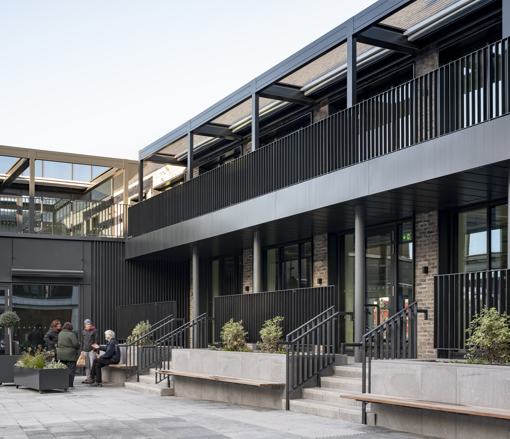 Raised concrete planters with metal railings and benches beneath a cantilevered walkway with exposed structure