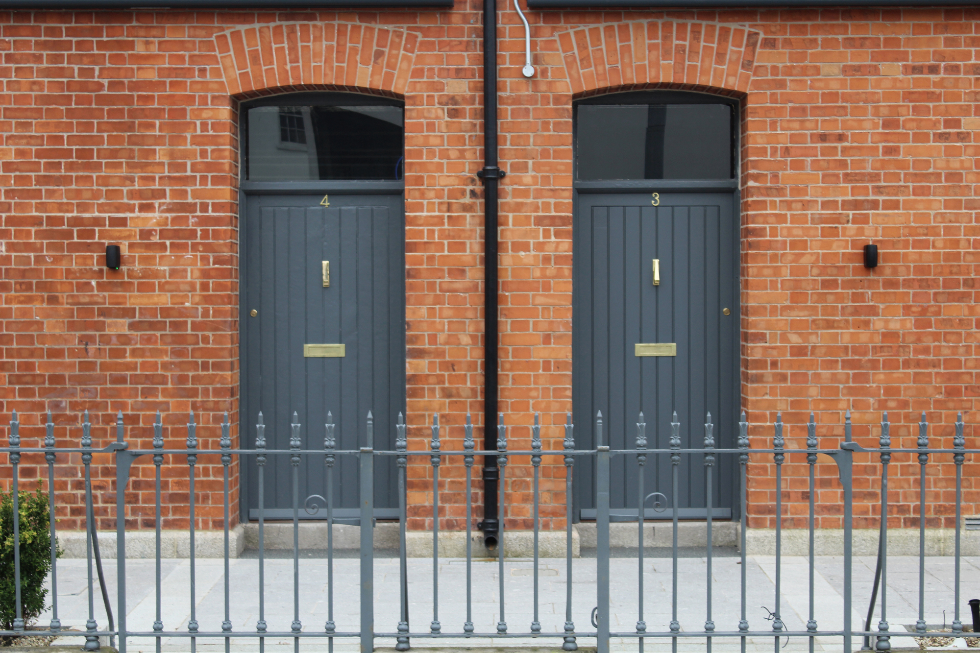 Two grey paneled entrance doors with arched transoms set in red brick facade behind metal railings