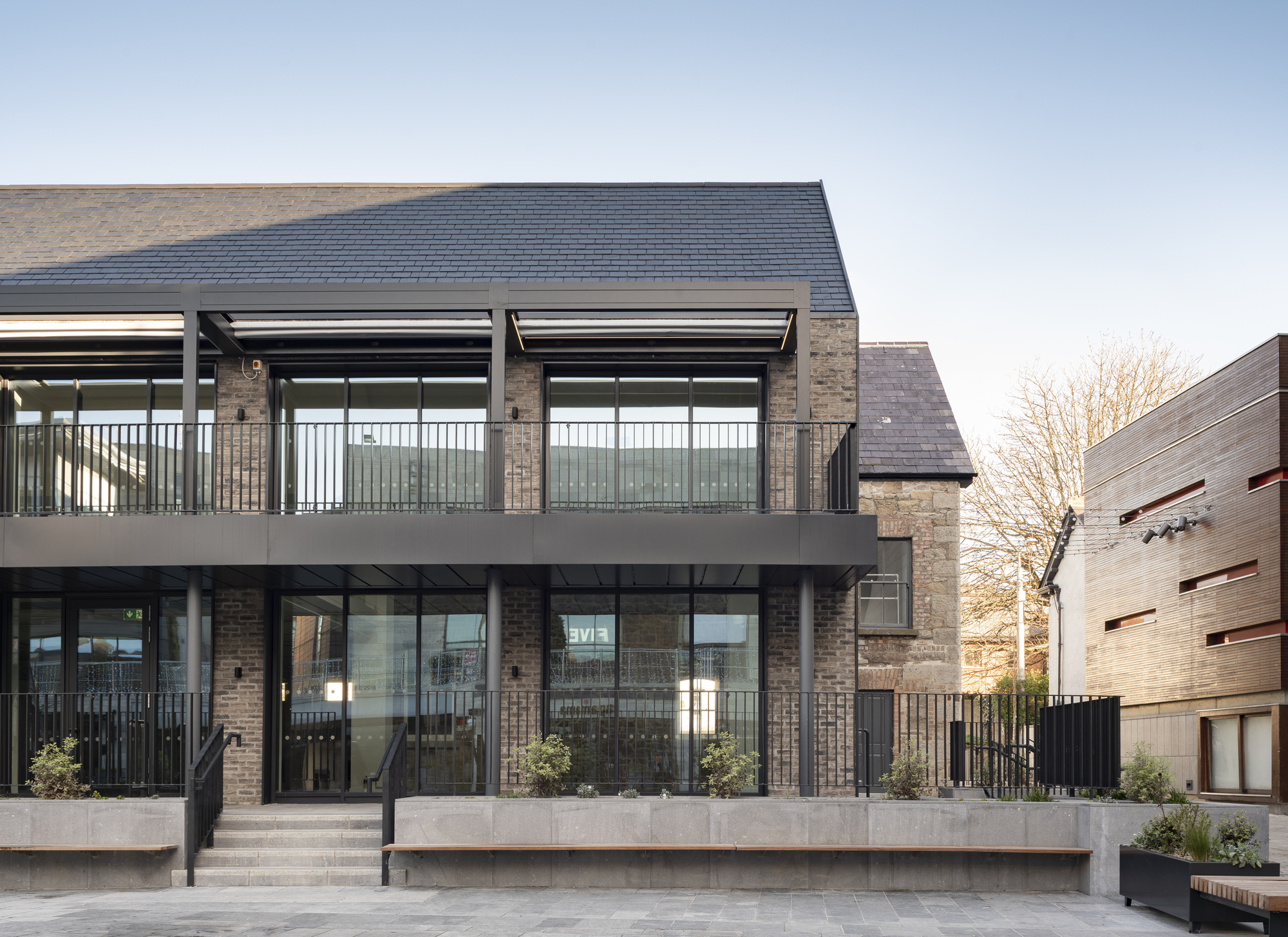Full-height glazed facade with clerestory windows and upper terrace railings beside a bare winter tree