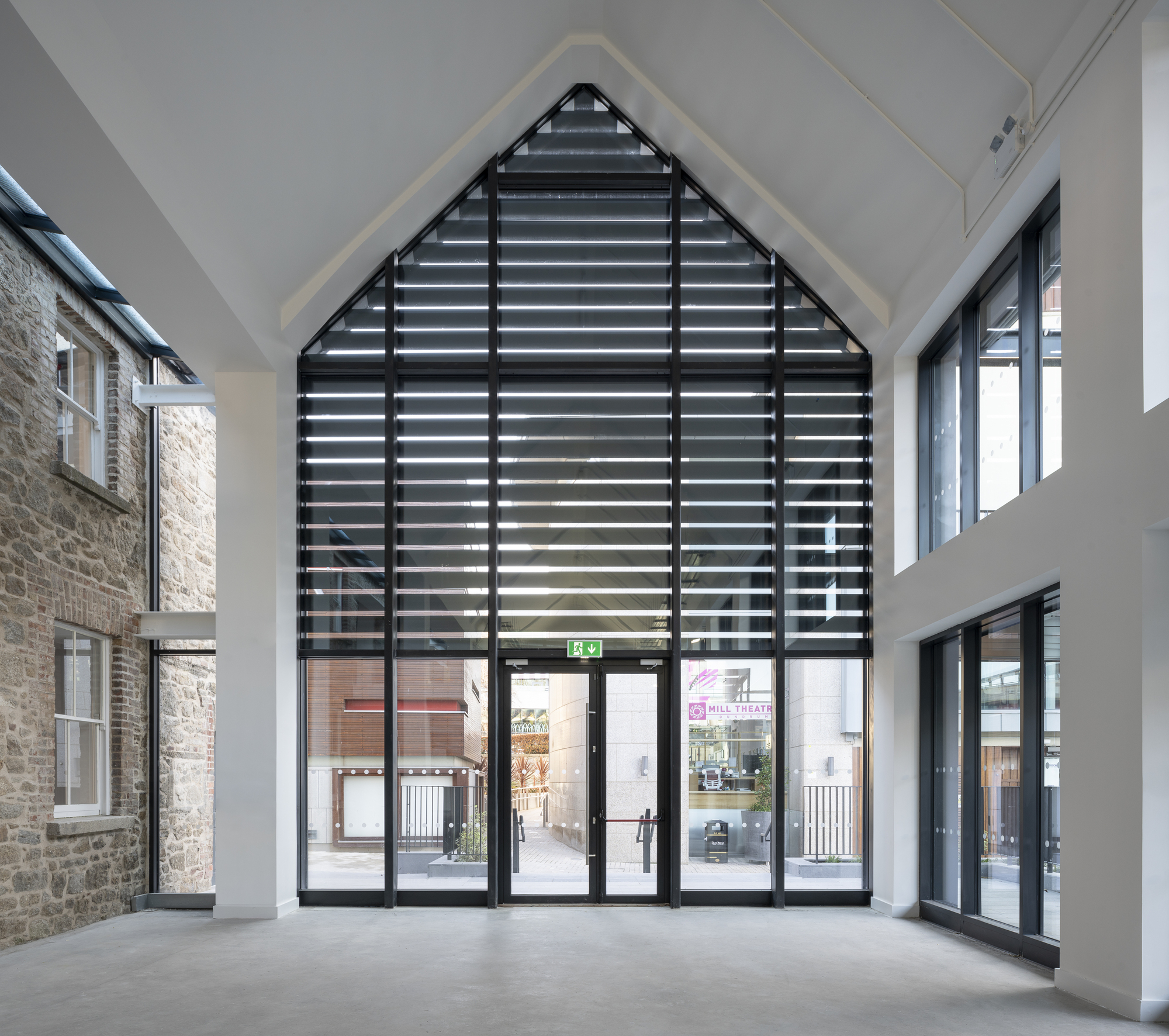 Interior view of gabled atrium with horizontal louvre screen and glazed doors opening to courtyard