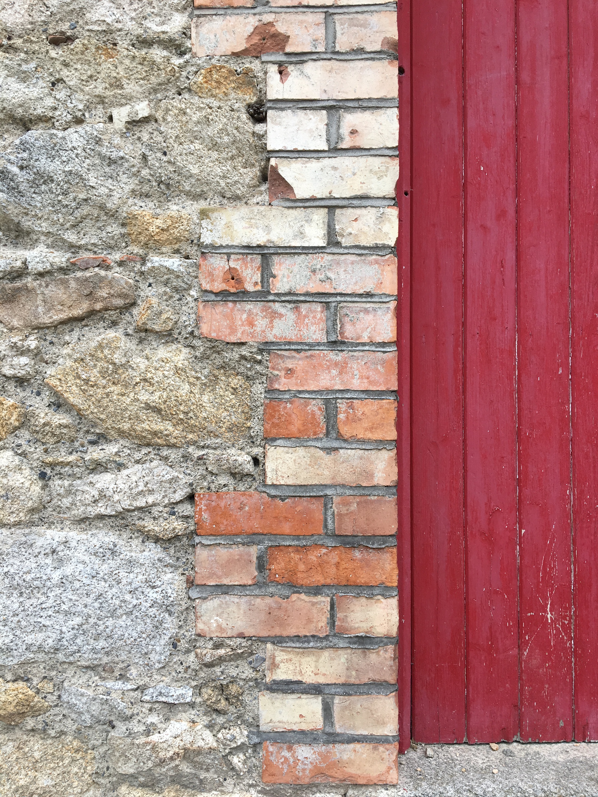 Detail of weathered stone wall meeting salvaged brick infill and painted timber door surround