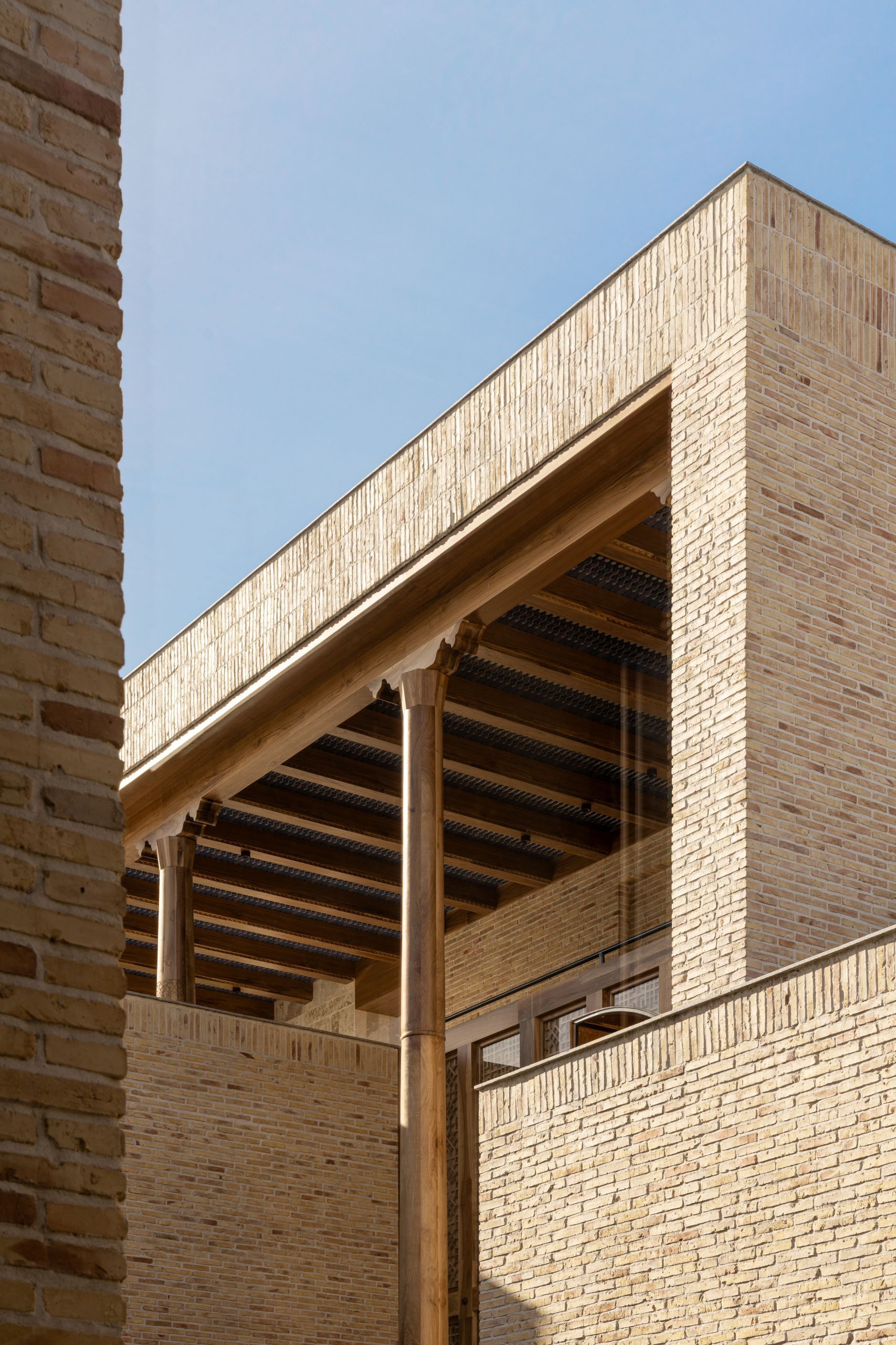 Close-up of the timber rafter structure framed within pale brick walls against a clear sky