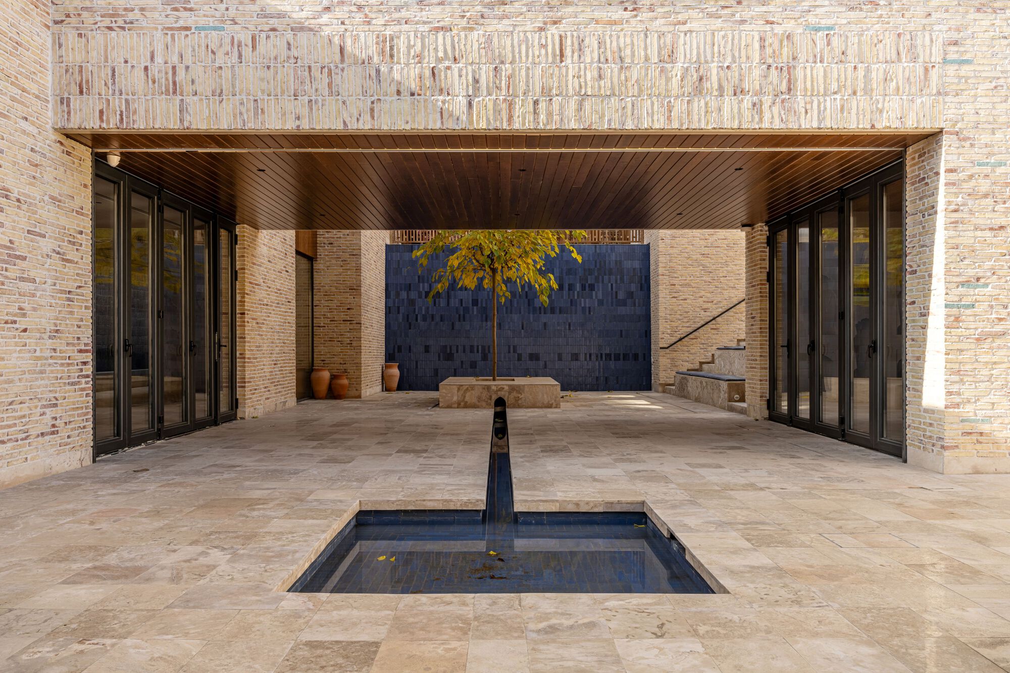 Covered courtyard with timber ceiling, reflecting pool, and folding glass doors