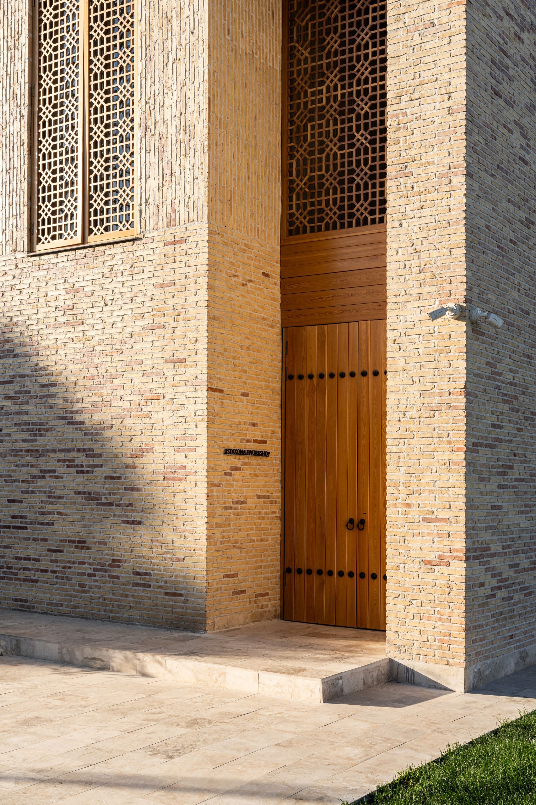 Tall wooden entrance door set within buff brick walls with decorative lattice screens above