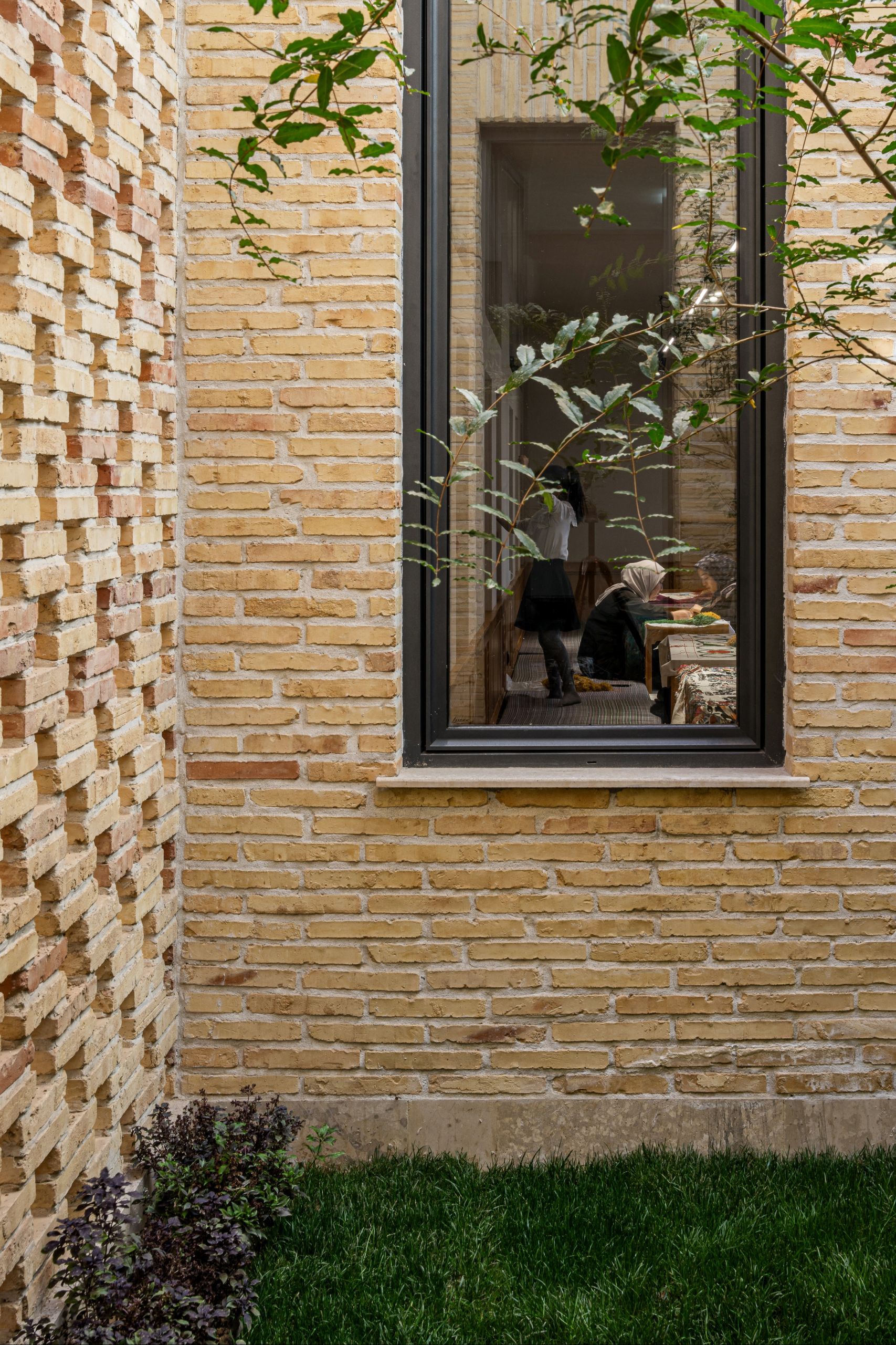 Textured brick facade with narrow vertical window framed in black metal and climbing greenery