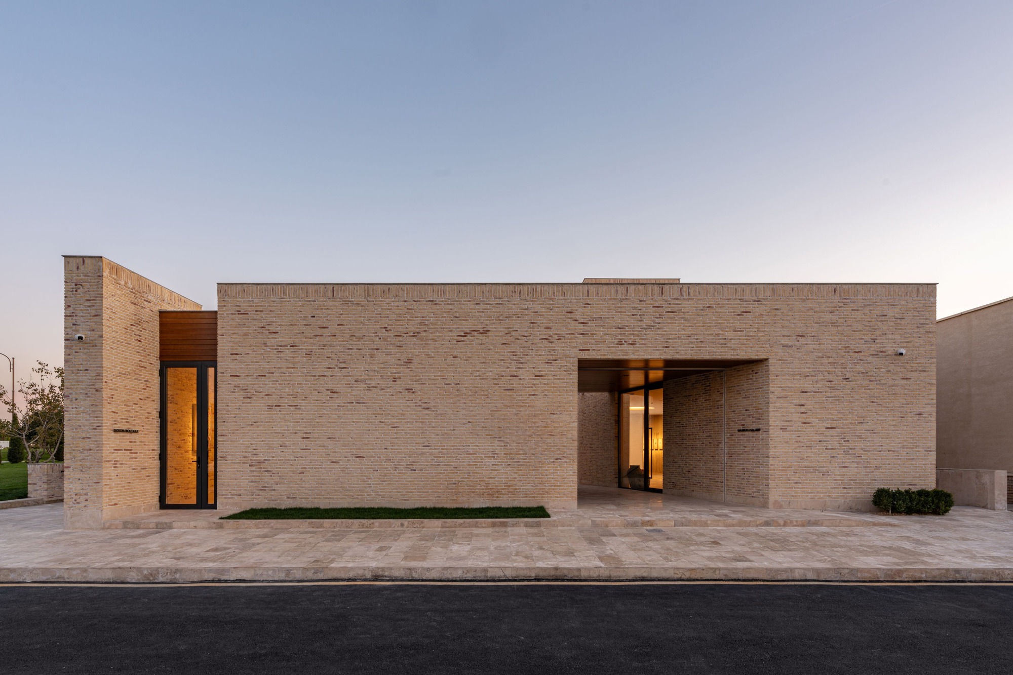 Street facade with variegated brick walls and recessed timber doorway under evening sky