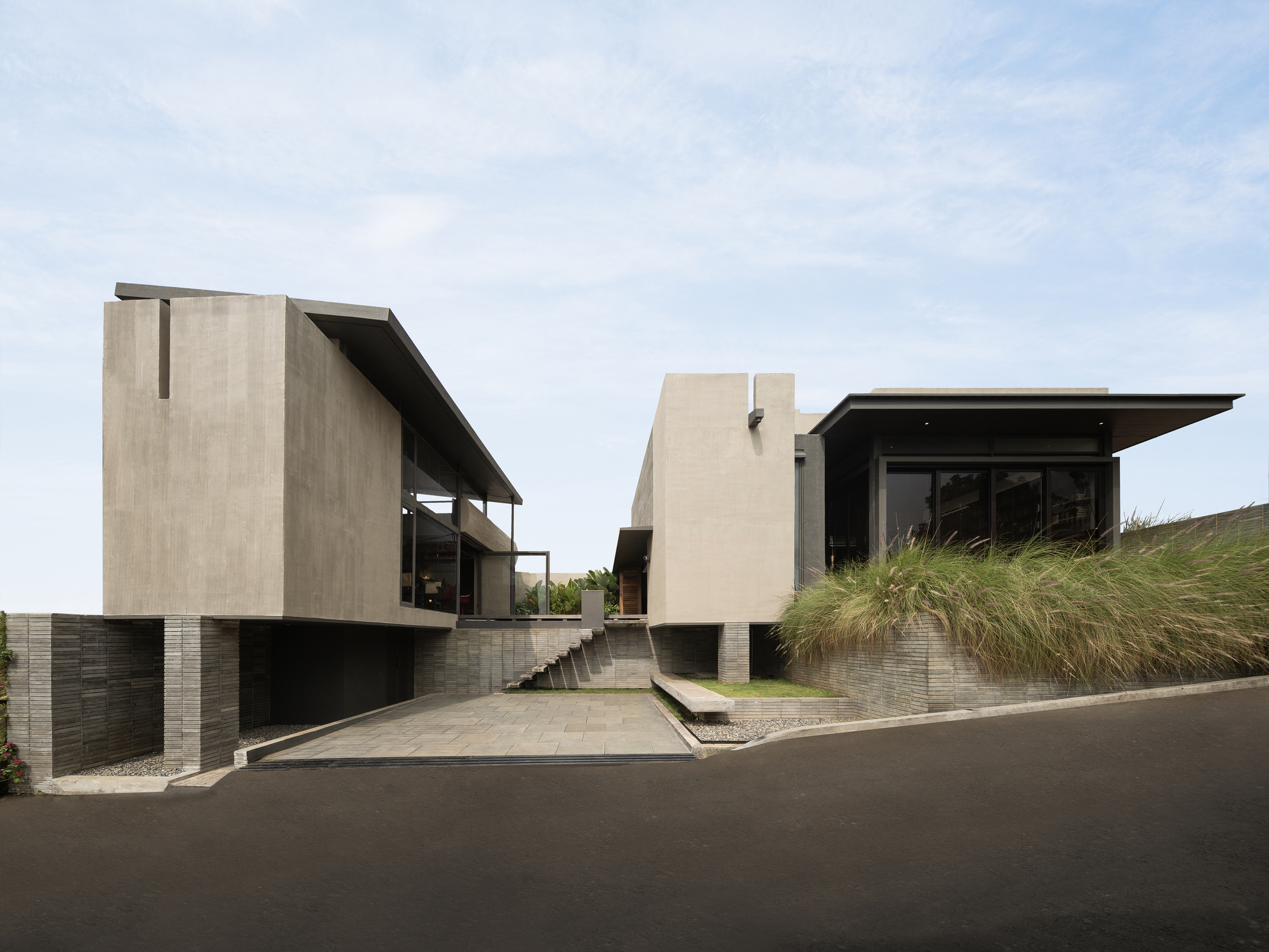 Street view of the split-level concrete volumes with cantilevered roofs and gravel courtyard between them