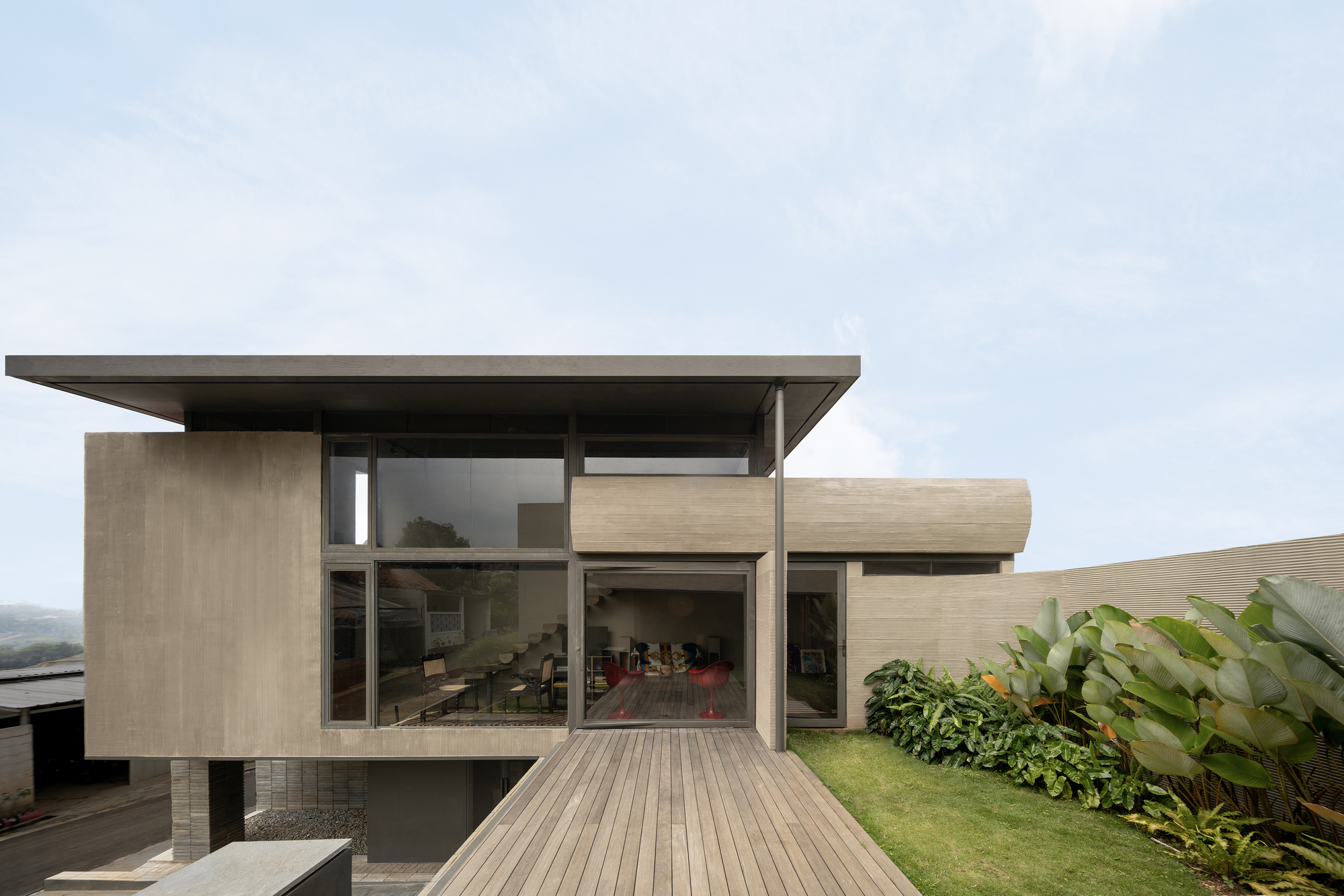 Garden facade with timber deck leading to the glass-walled living room beneath a flat roof overhang