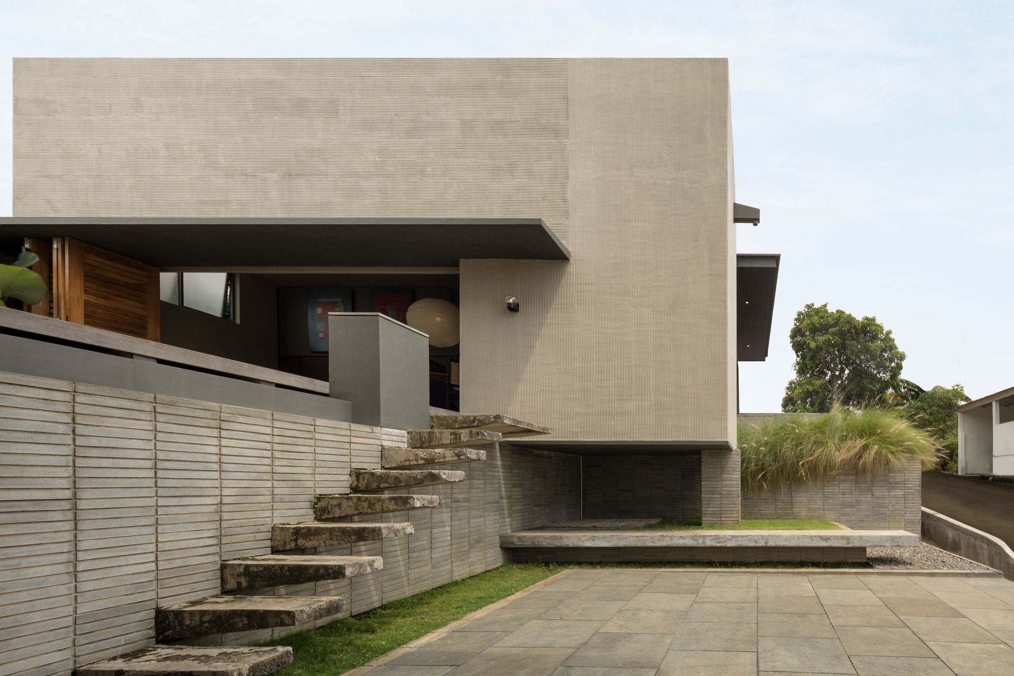 Concrete staircase climbing the exterior wall beside horizontal louvered screens and a lawn patch