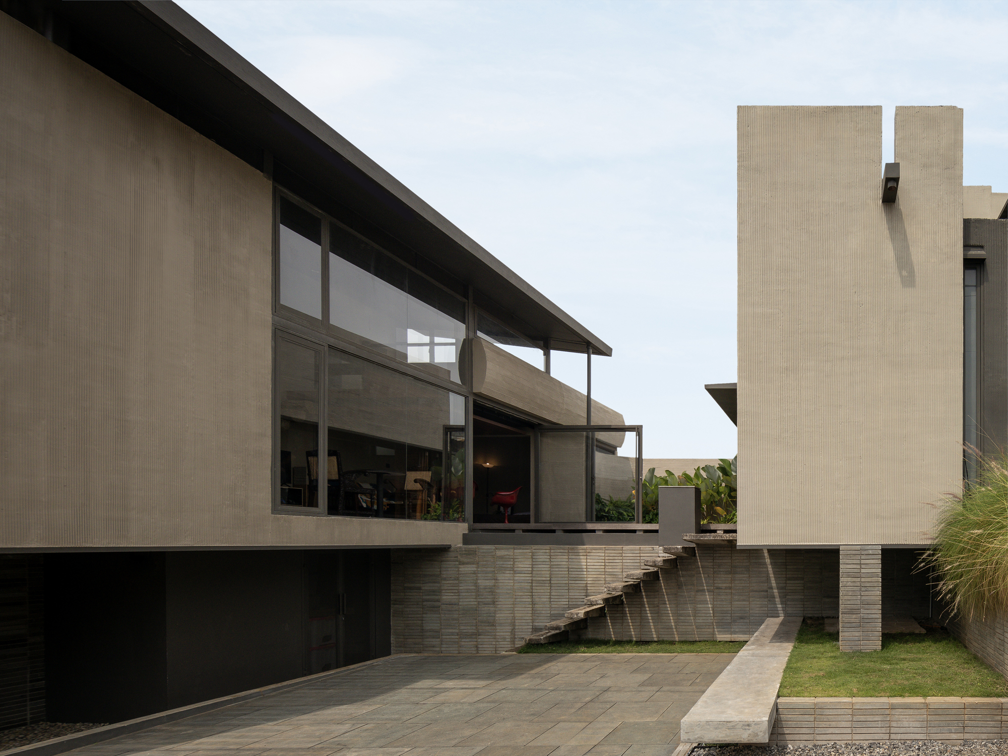 Rear elevation showing glazed volumes elevated on striped masonry plinths with sloping lawn below