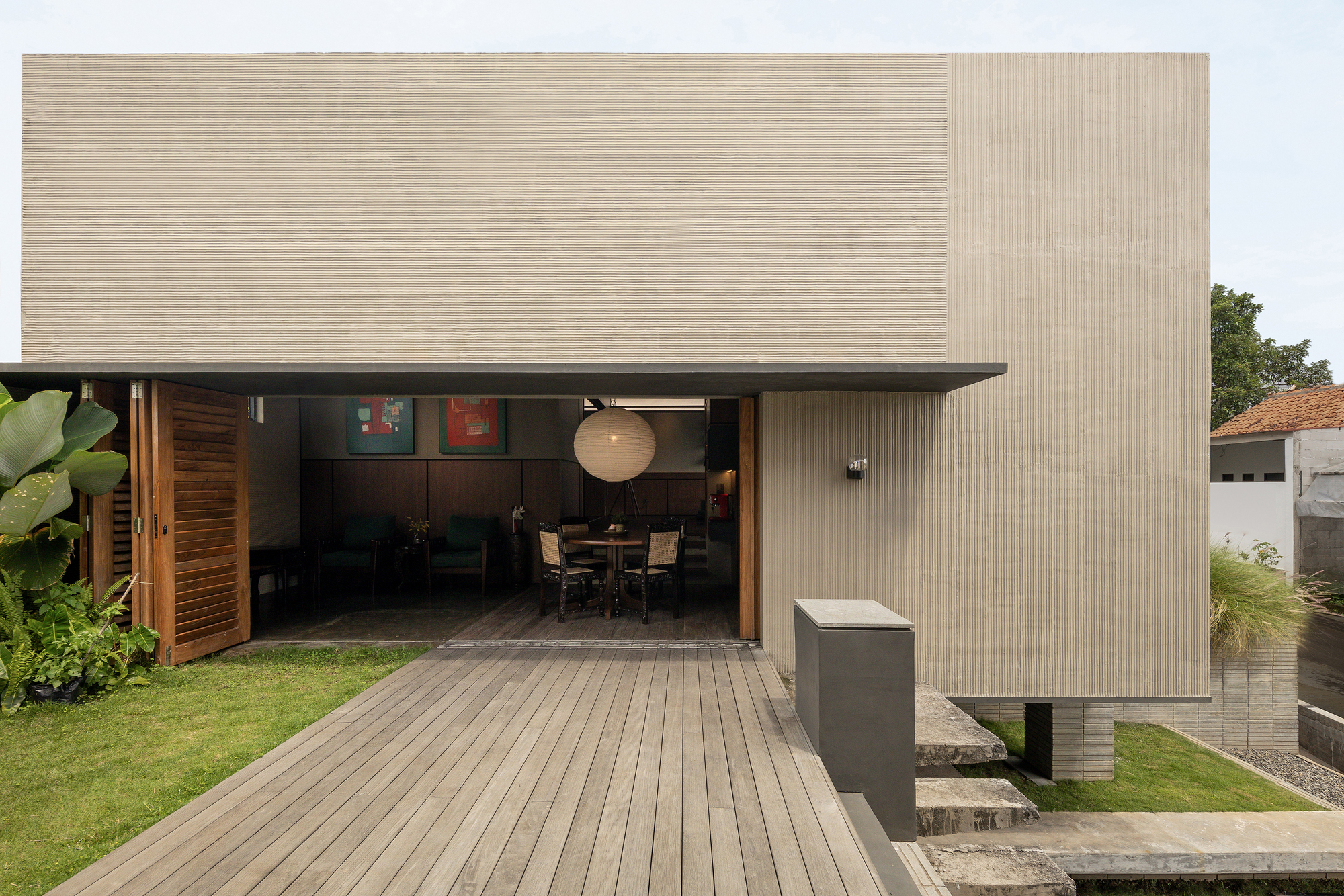 Timber deck leading to an open living area framed by vertical wood slats and tropical plants