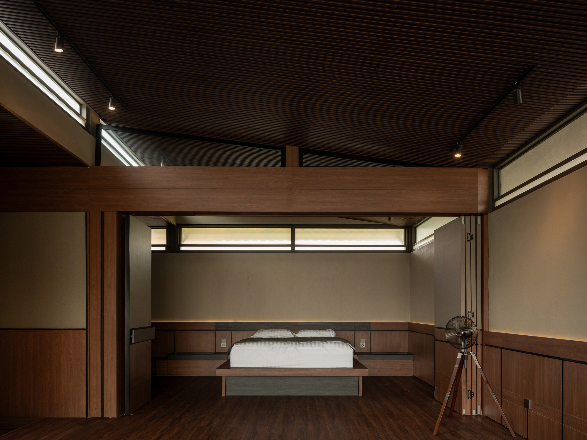Bedroom with timber bed platform below mezzanine and horizontal clerestory windows with slatted ceiling