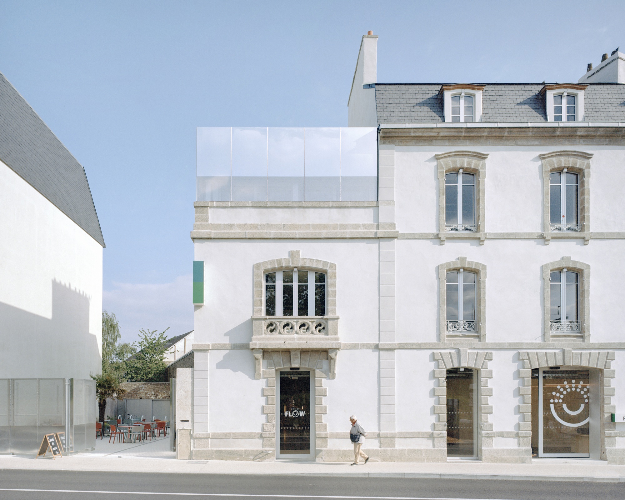Street facade showing white-painted stone building with arched windows and translucent panel addition above