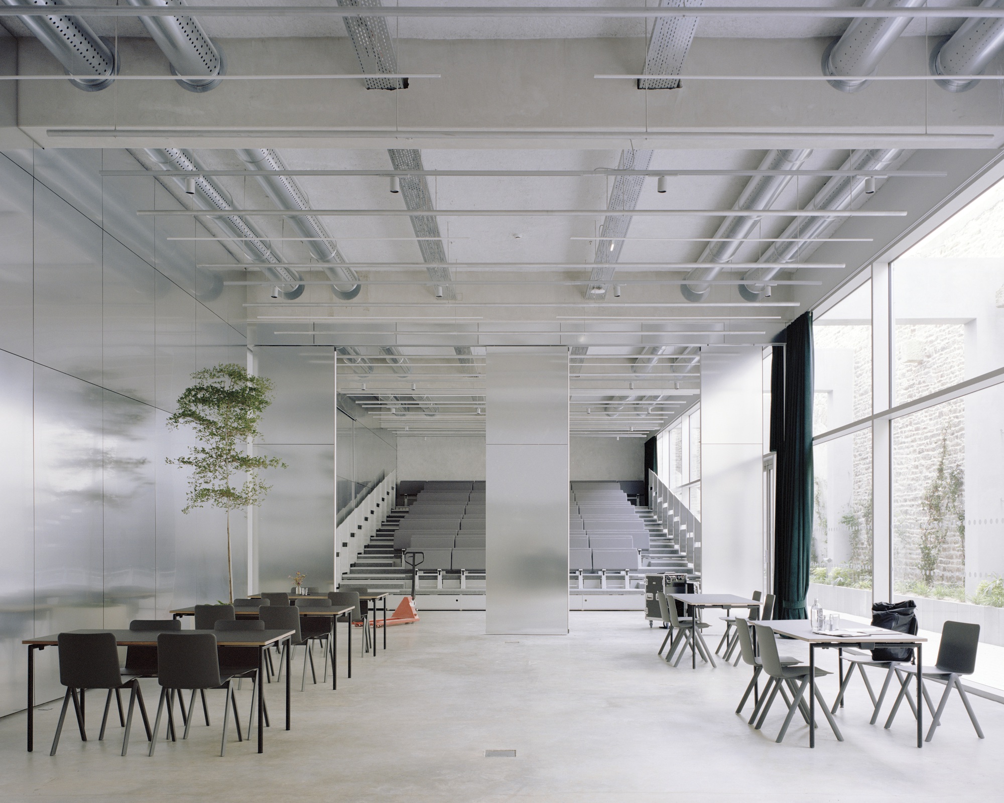 Interior foyer with exposed ceiling ducts, polished concrete floor, seating areas and twin staircases beyond
