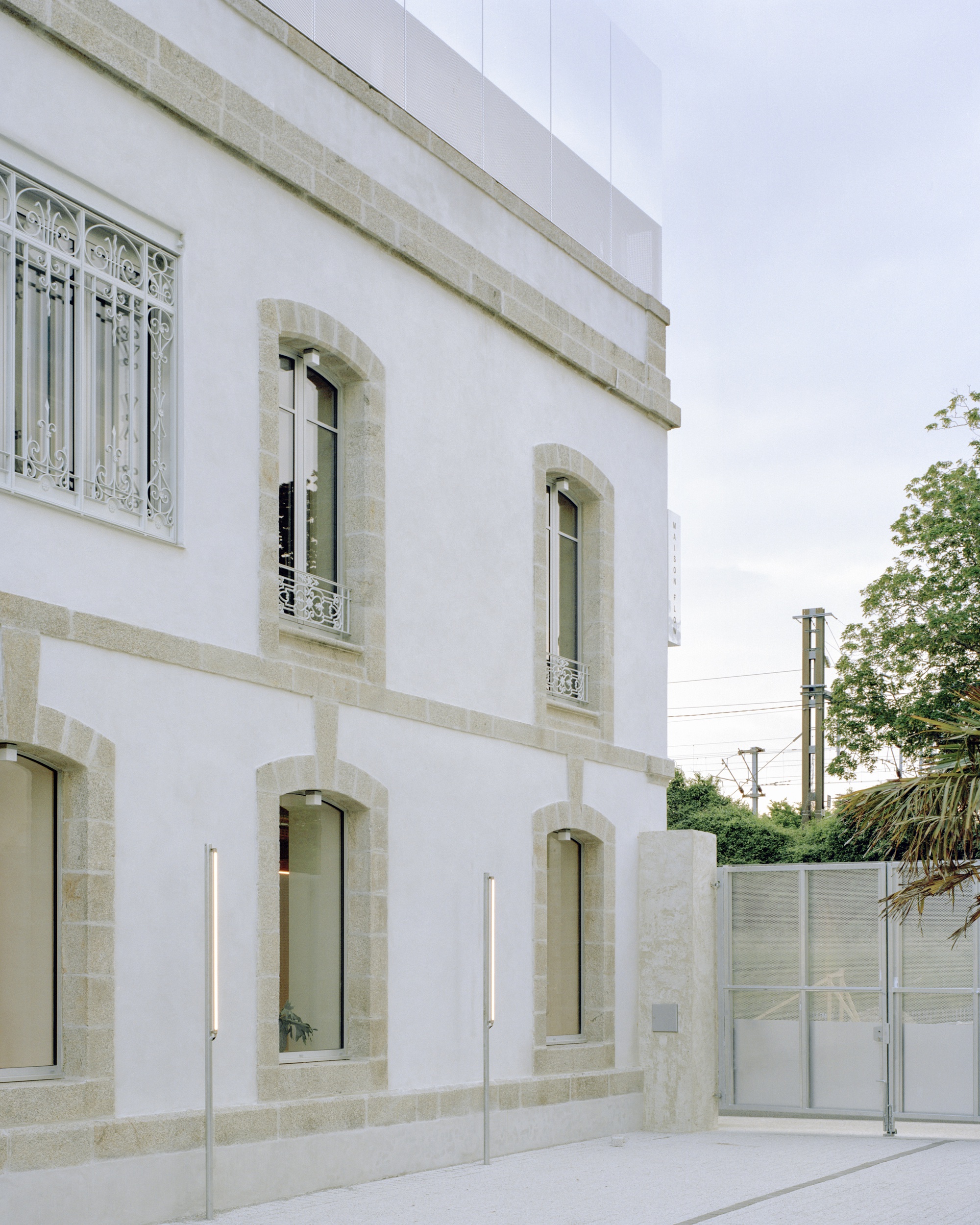 White stucco facade with stone-framed arched windows and decorative wrought iron grilles under an overcast sky