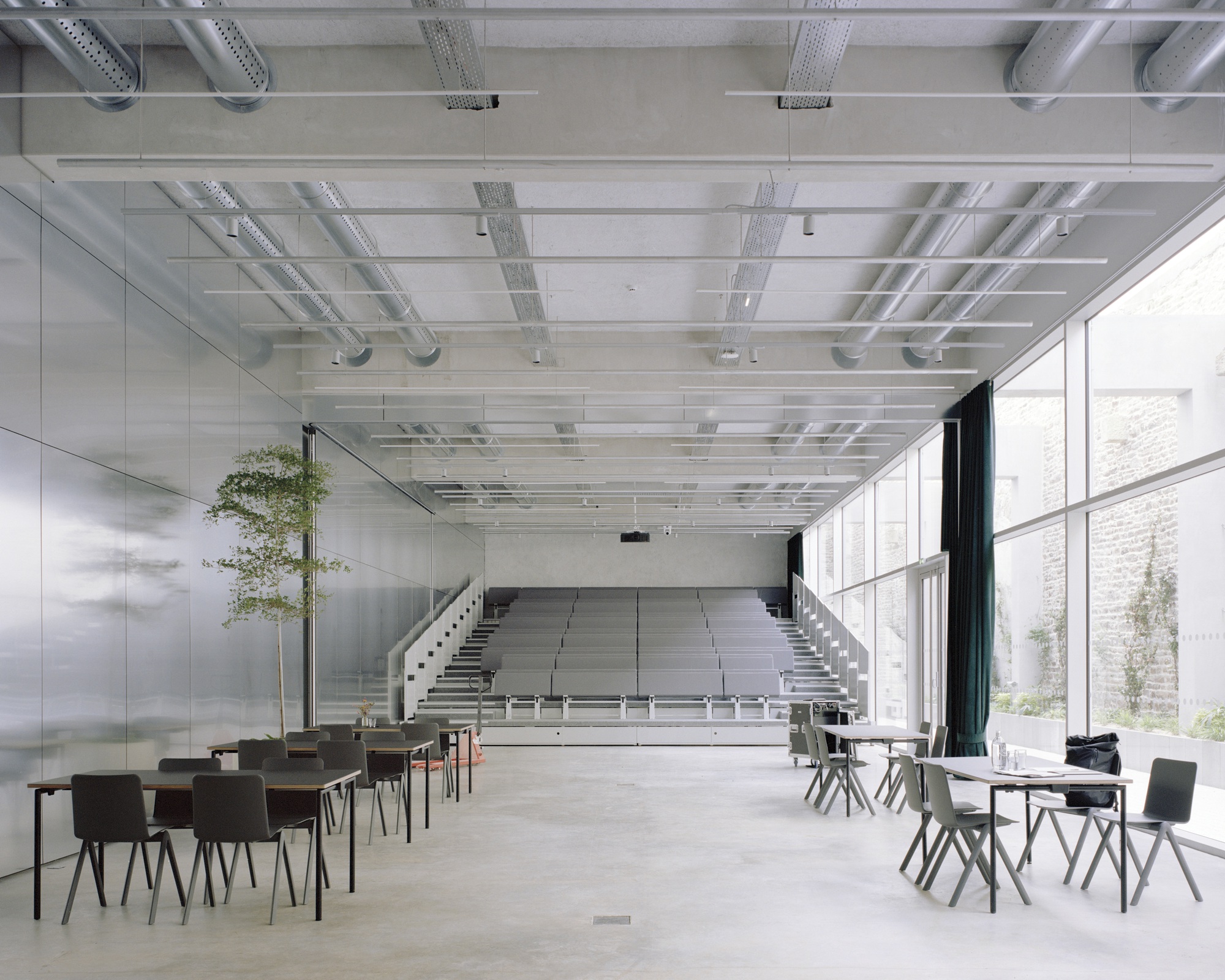 Retractable tiered seating emerging from the floor beneath a gridded ceiling with exposed mechanical systems
