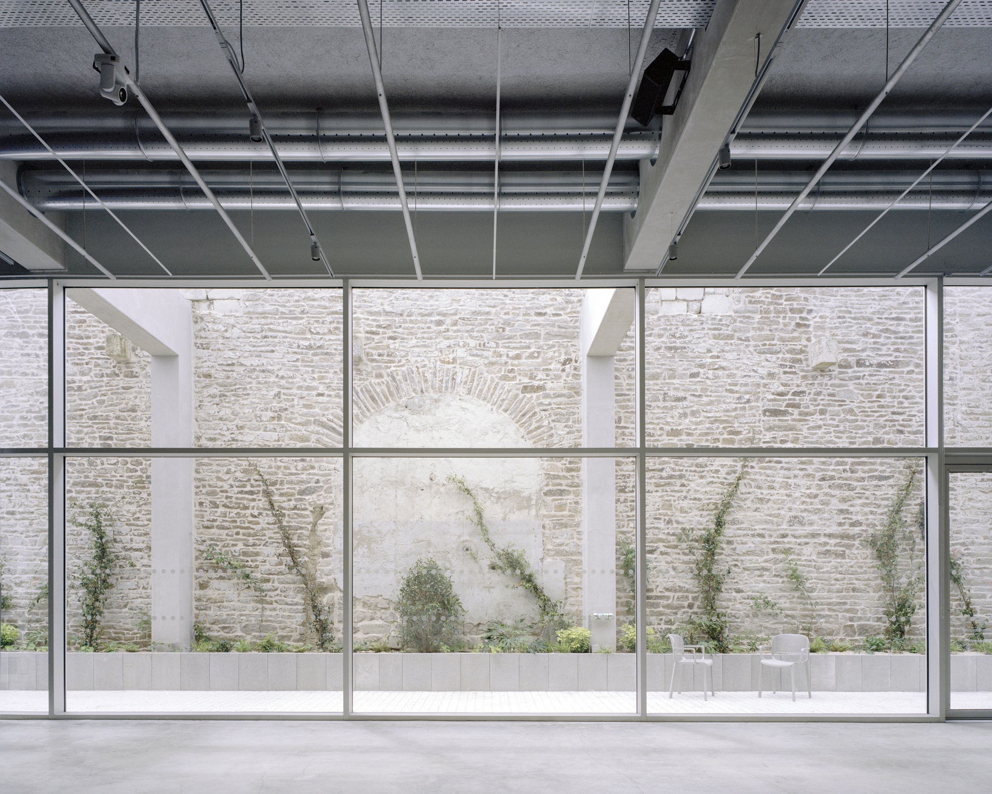 Floor-to-ceiling glazing framing a limestone courtyard wall with climbing vines and a bricked arch