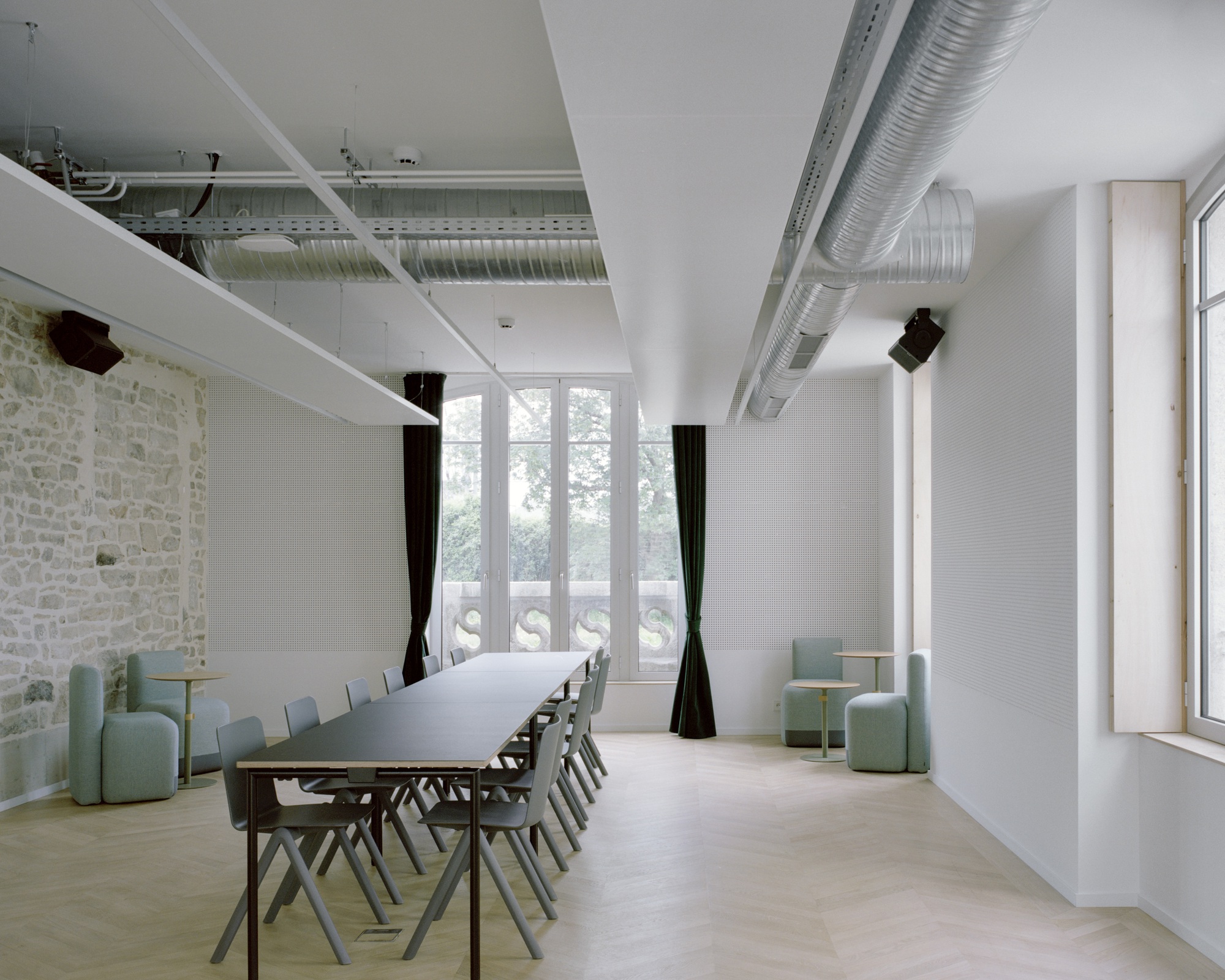 Meeting room with exposed stone wall, suspended ductwork, long white table, and green upholstered seating