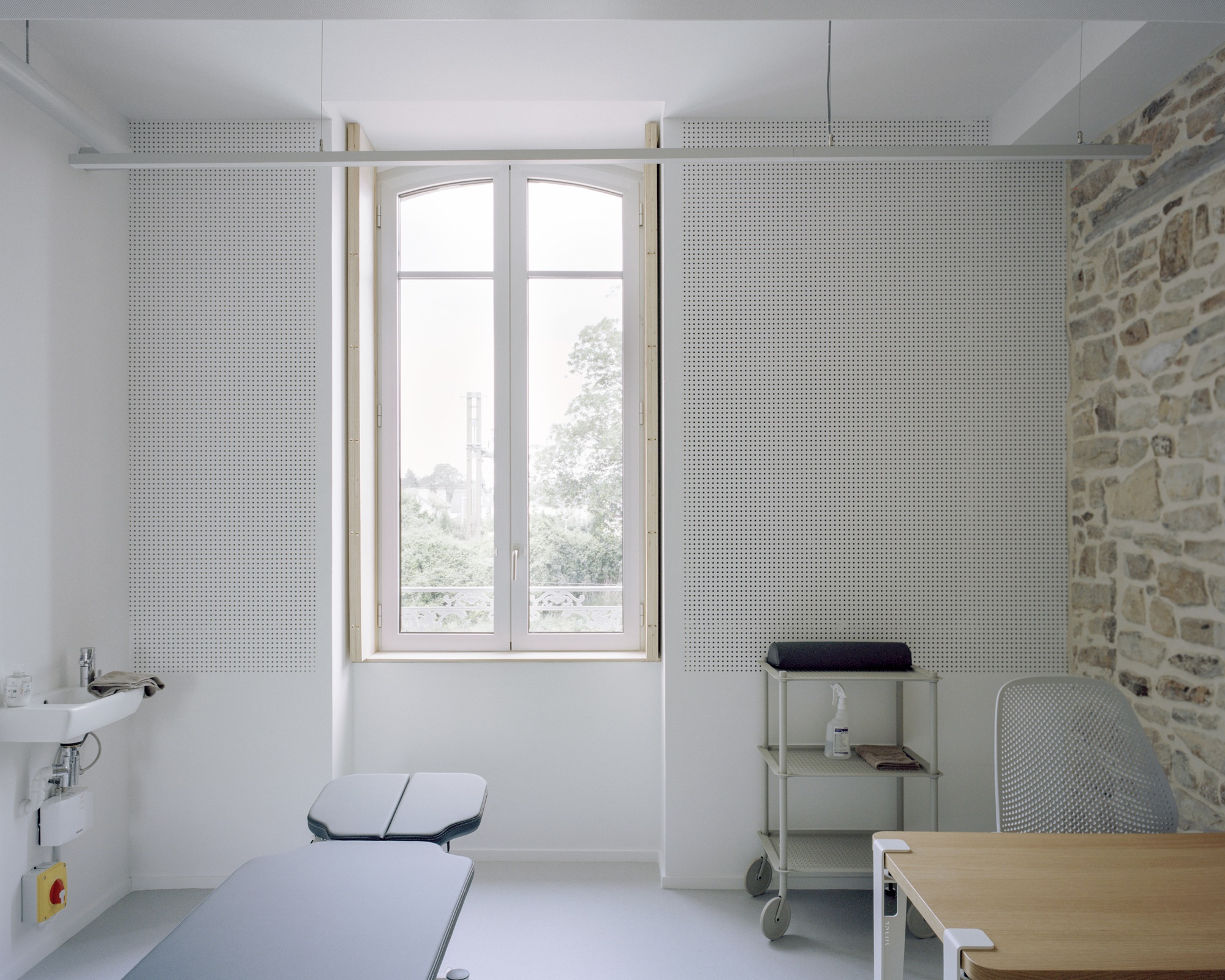 Interior workspace with perforated sliding panels flanking an arched window overlooking a courtyard with trees
