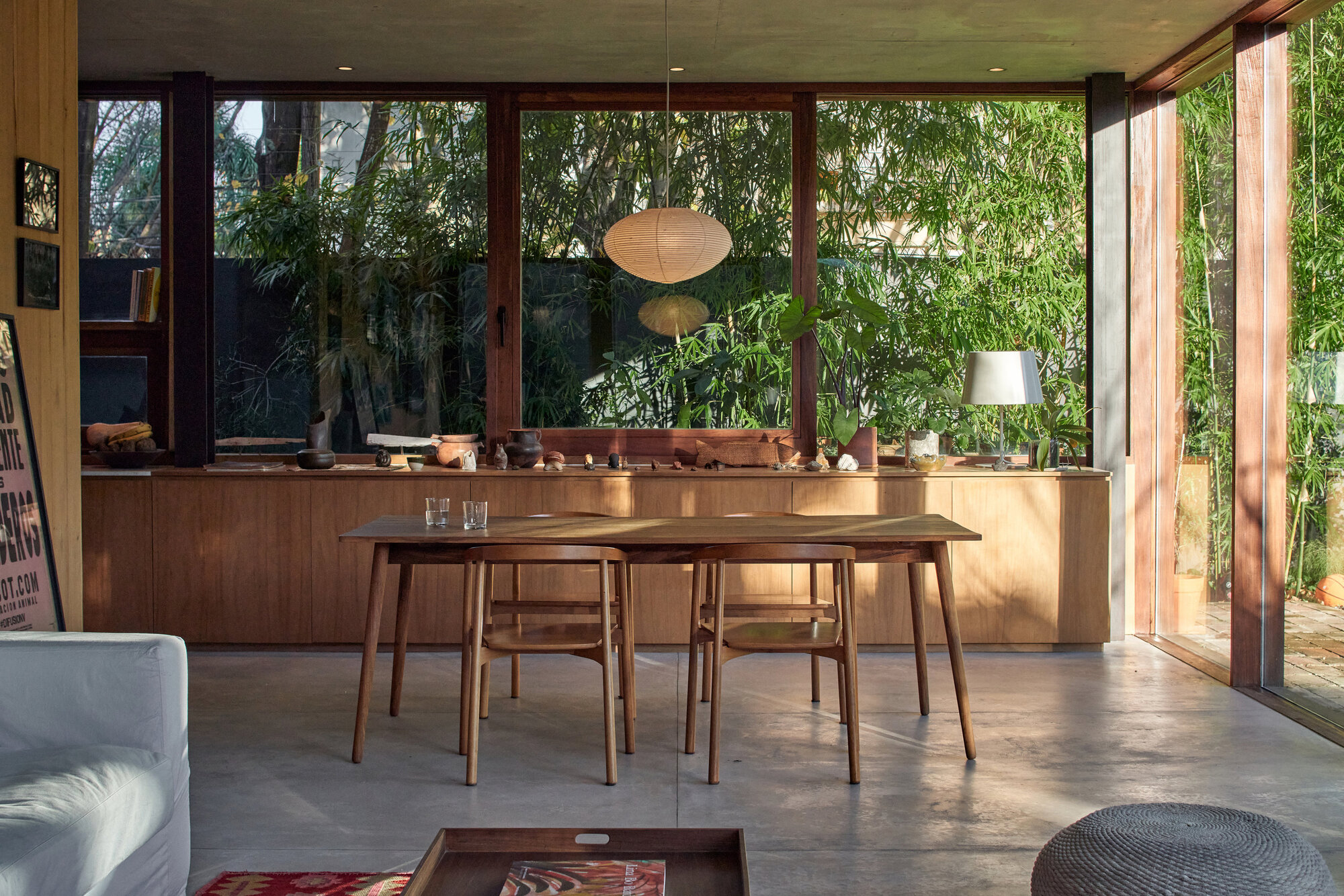 Open plan dining area with timber table and floor-to-ceiling glazing overlooking planted vegetation