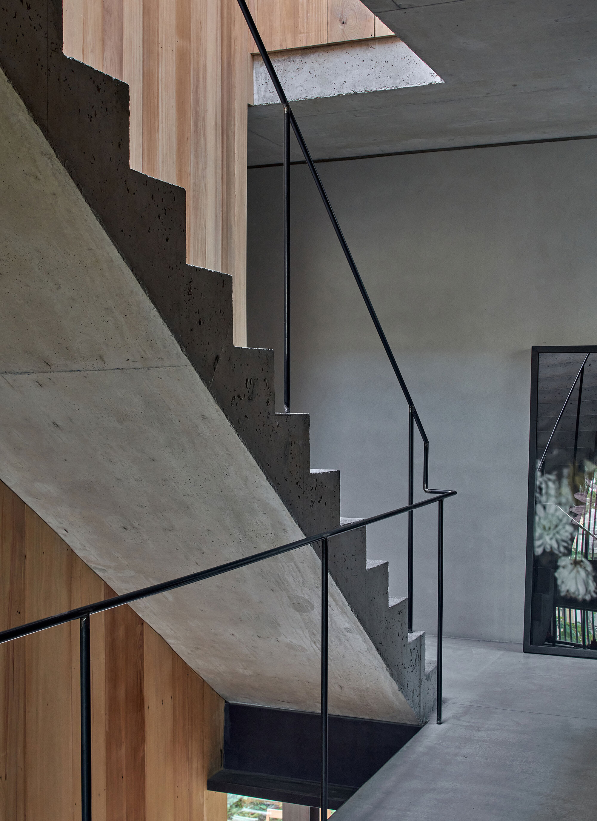 Close-up of cantilevered concrete stair treads with minimal black steel handrail against timber cladding