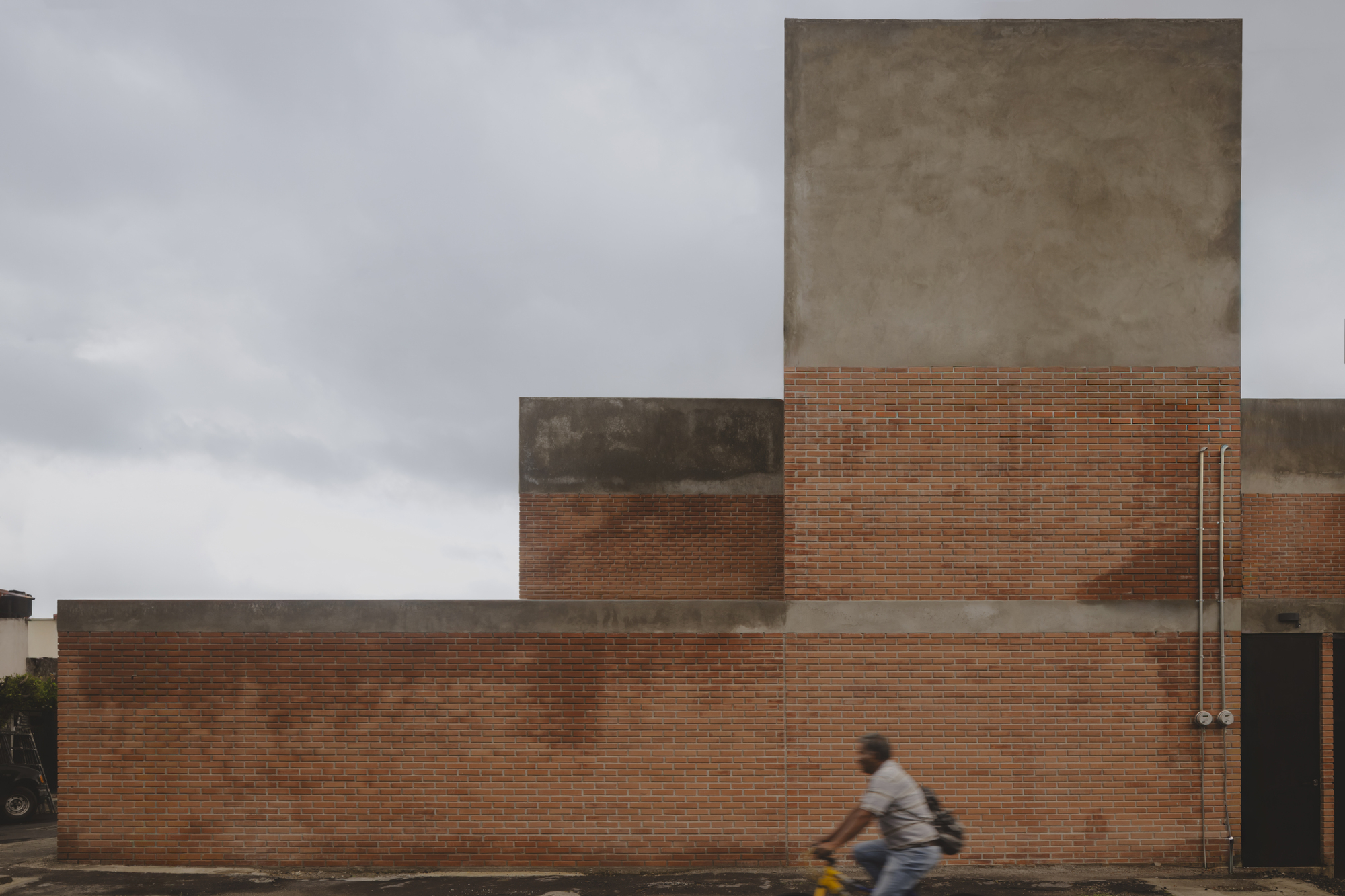 Street elevation of layered brick and concrete volumes with a cyclist passing by