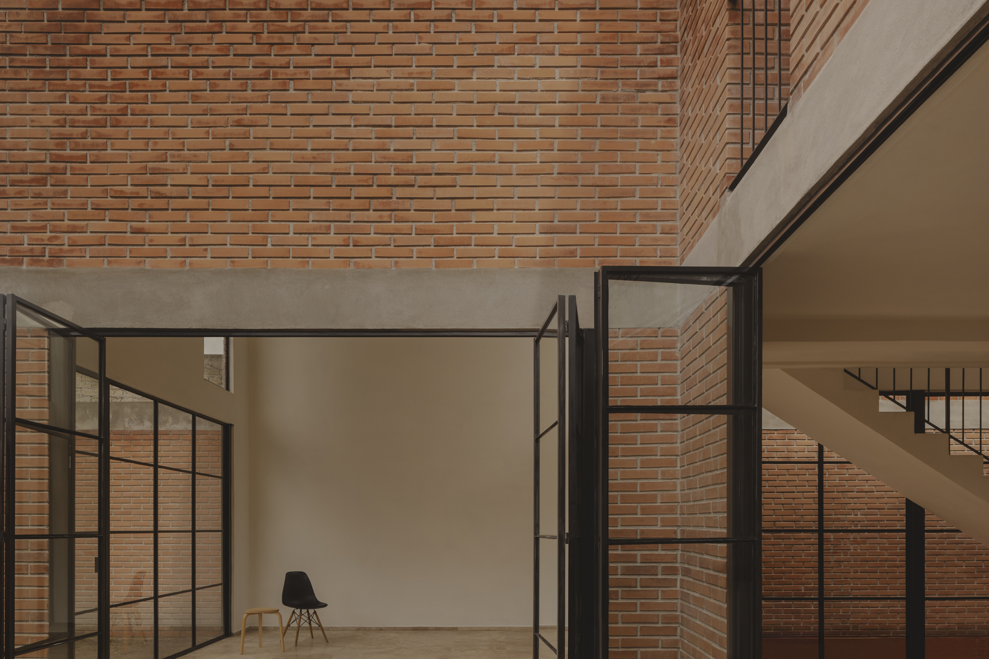 Steel-framed opening to a room with a single black chair against exposed brick walls