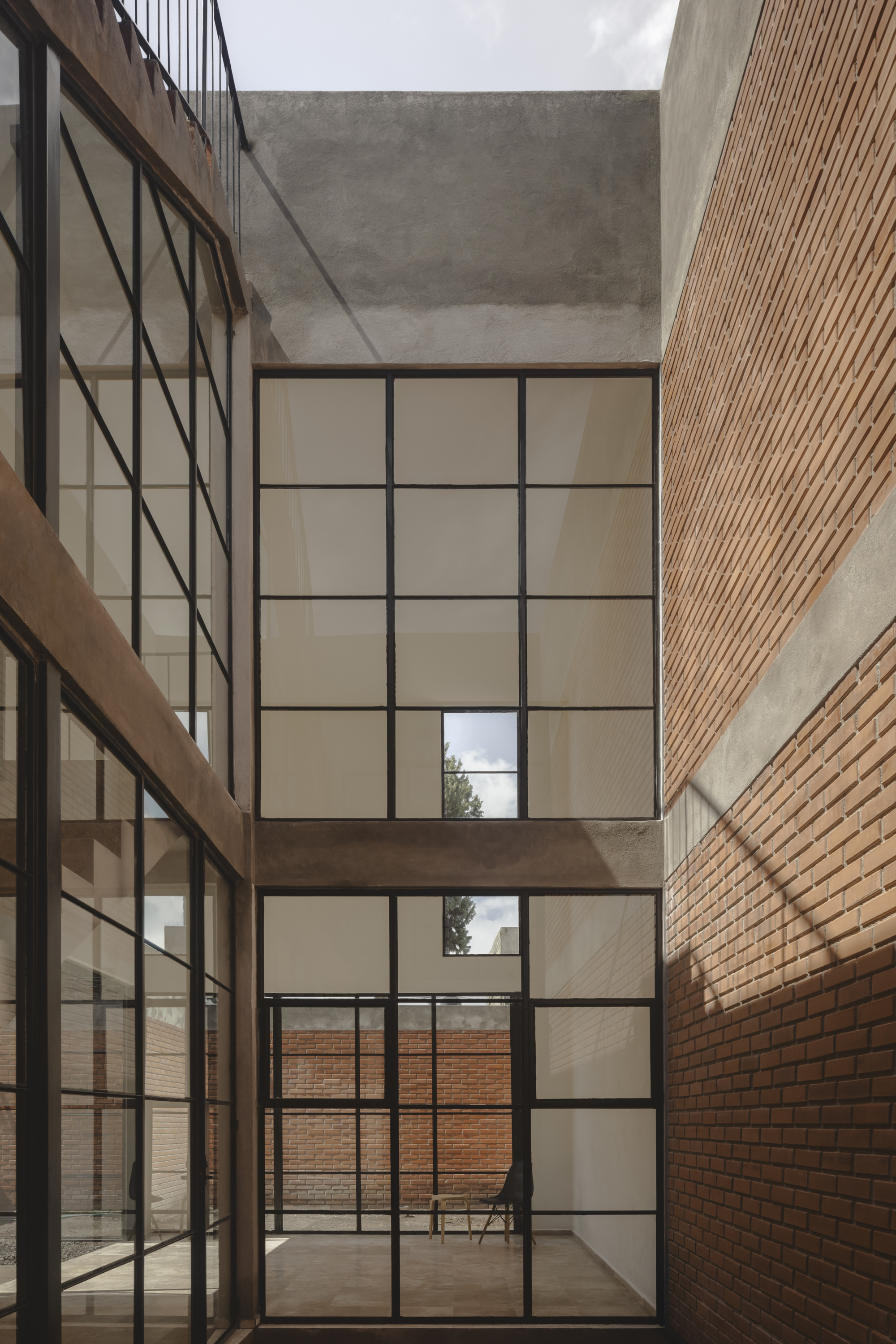 Vertical courtyard with stacked steel-framed windows between brick and concrete surfaces