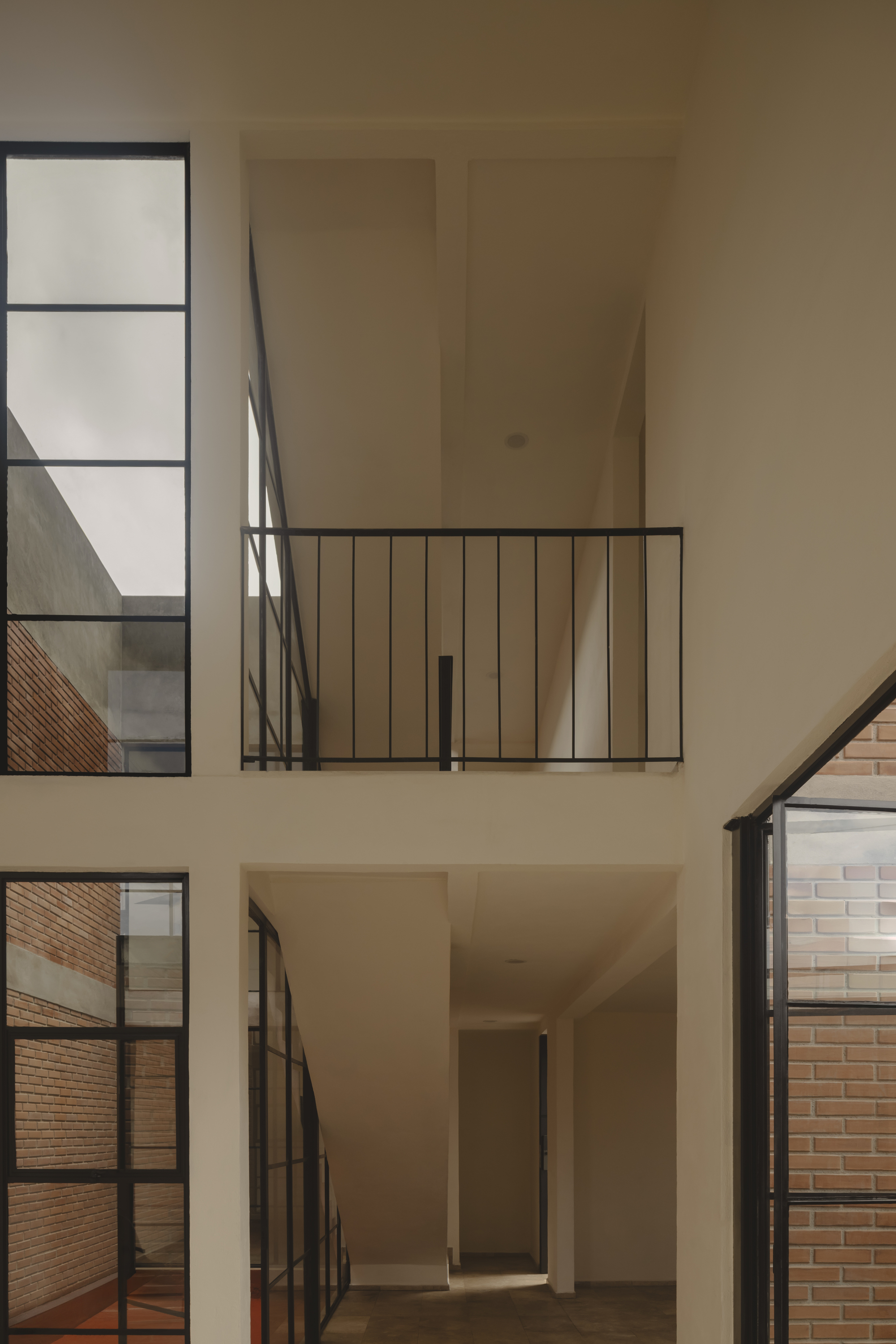 Double-height interior void with black steel framed windows and railings overlooking brick walls