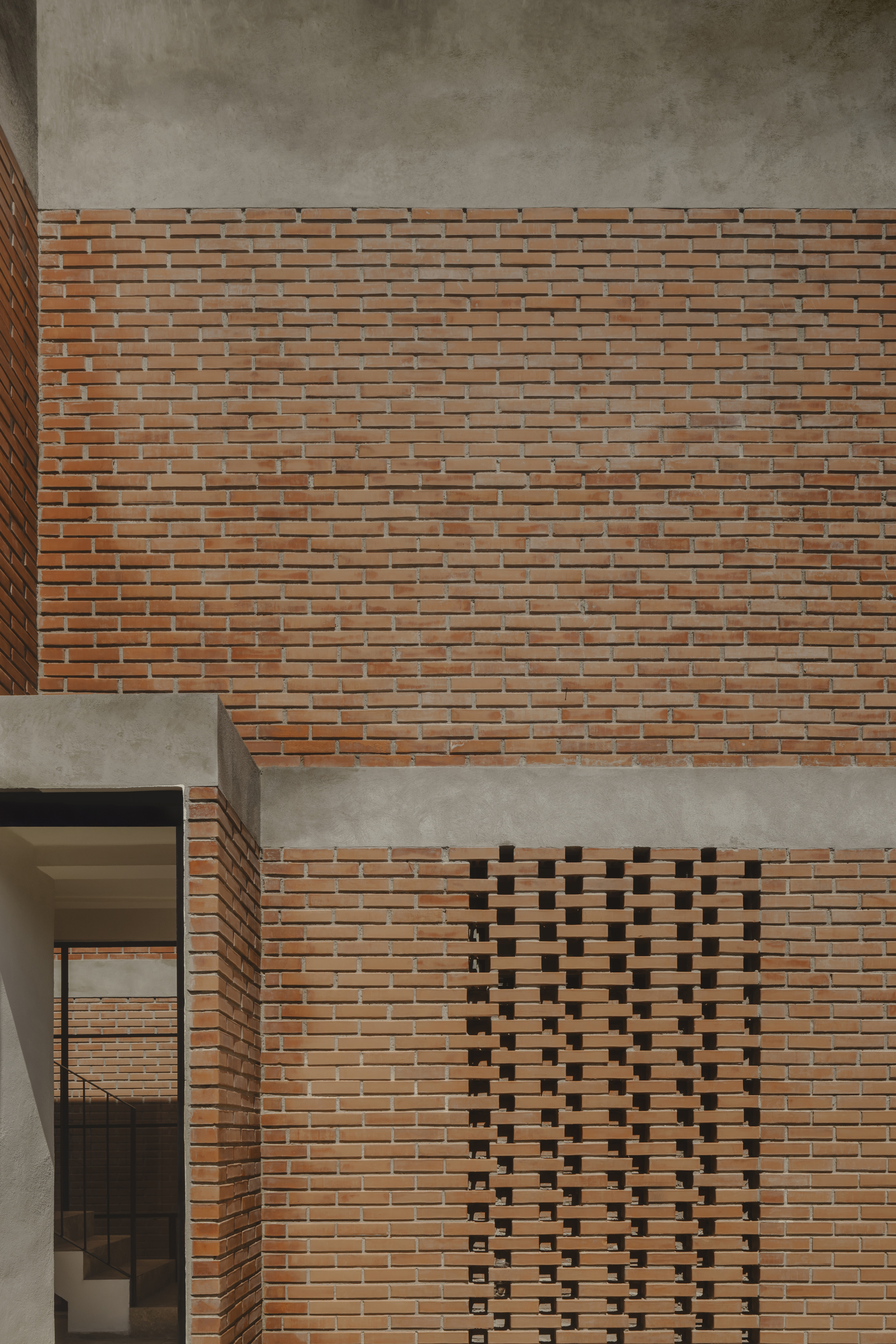 Brick facade detail with patterned ventilation opening and concrete band wrapping the corner balcony