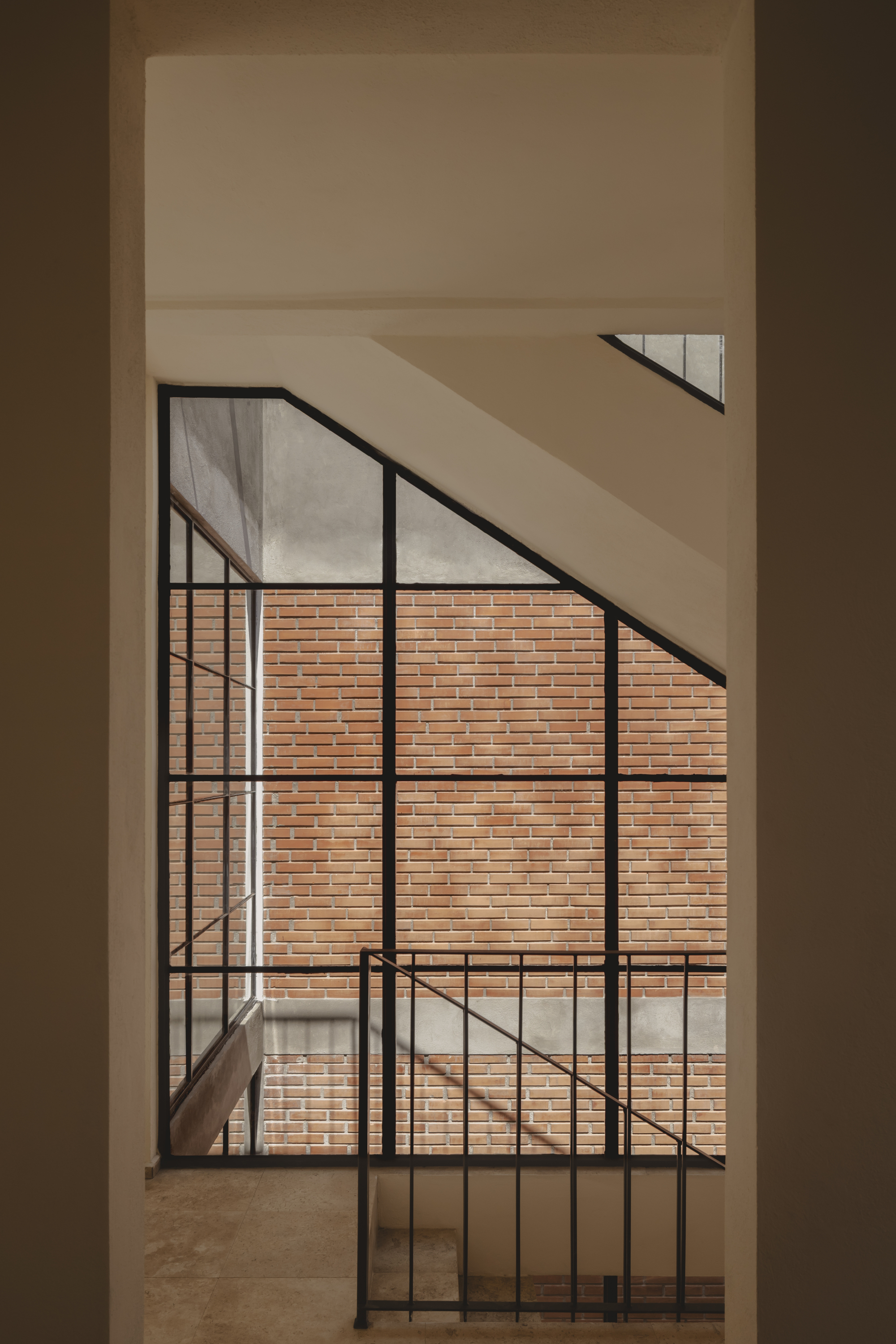 Black steel framed window casting diagonal shadows across white interior walls facing brick courtyard