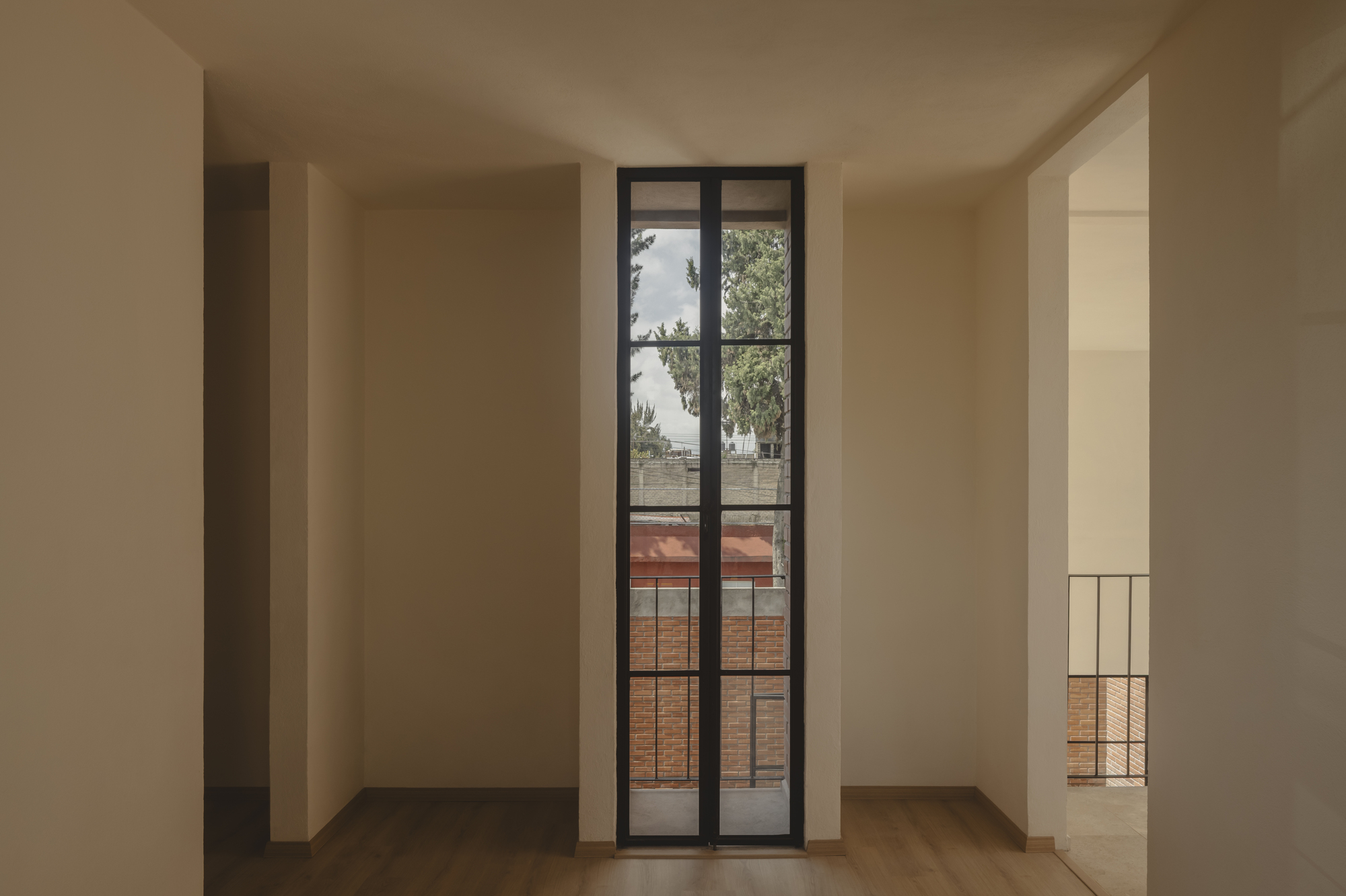 Interior room with tall steel framed door opening to balcony overlooking tree canopy and brick rooftops