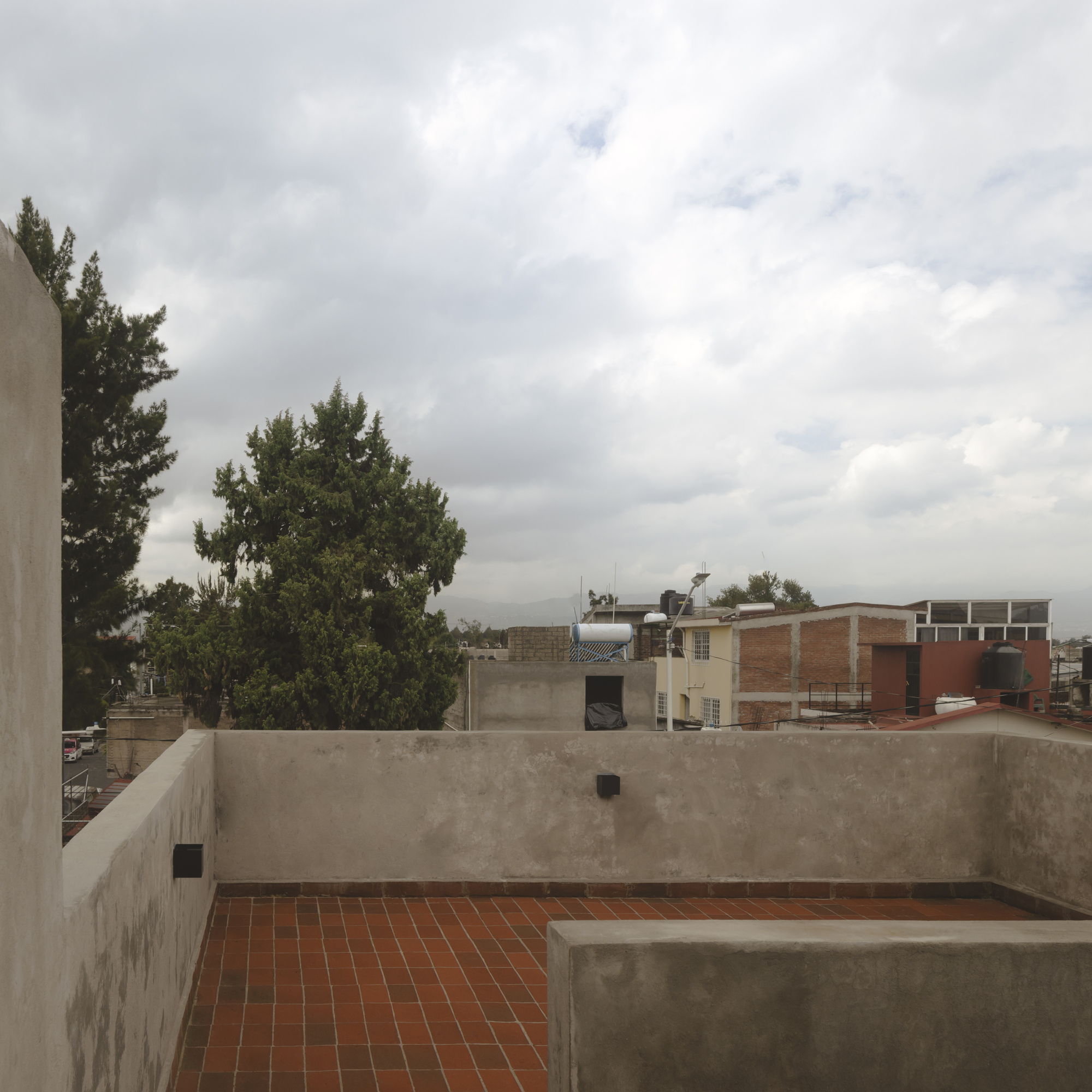 Rooftop terrace with red clay tile flooring and concrete parapet walls under overcast sky