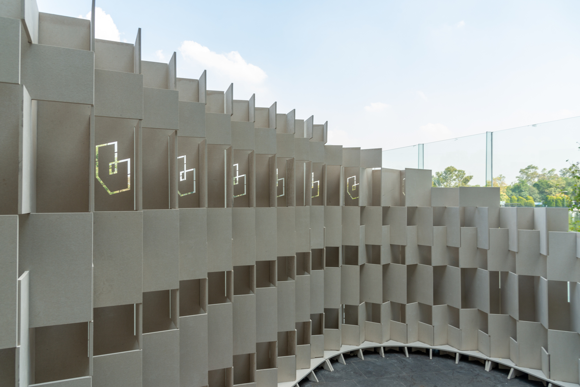 Modular gray concrete screen wall with integrated apertures and illuminated geometric symbols in daylight