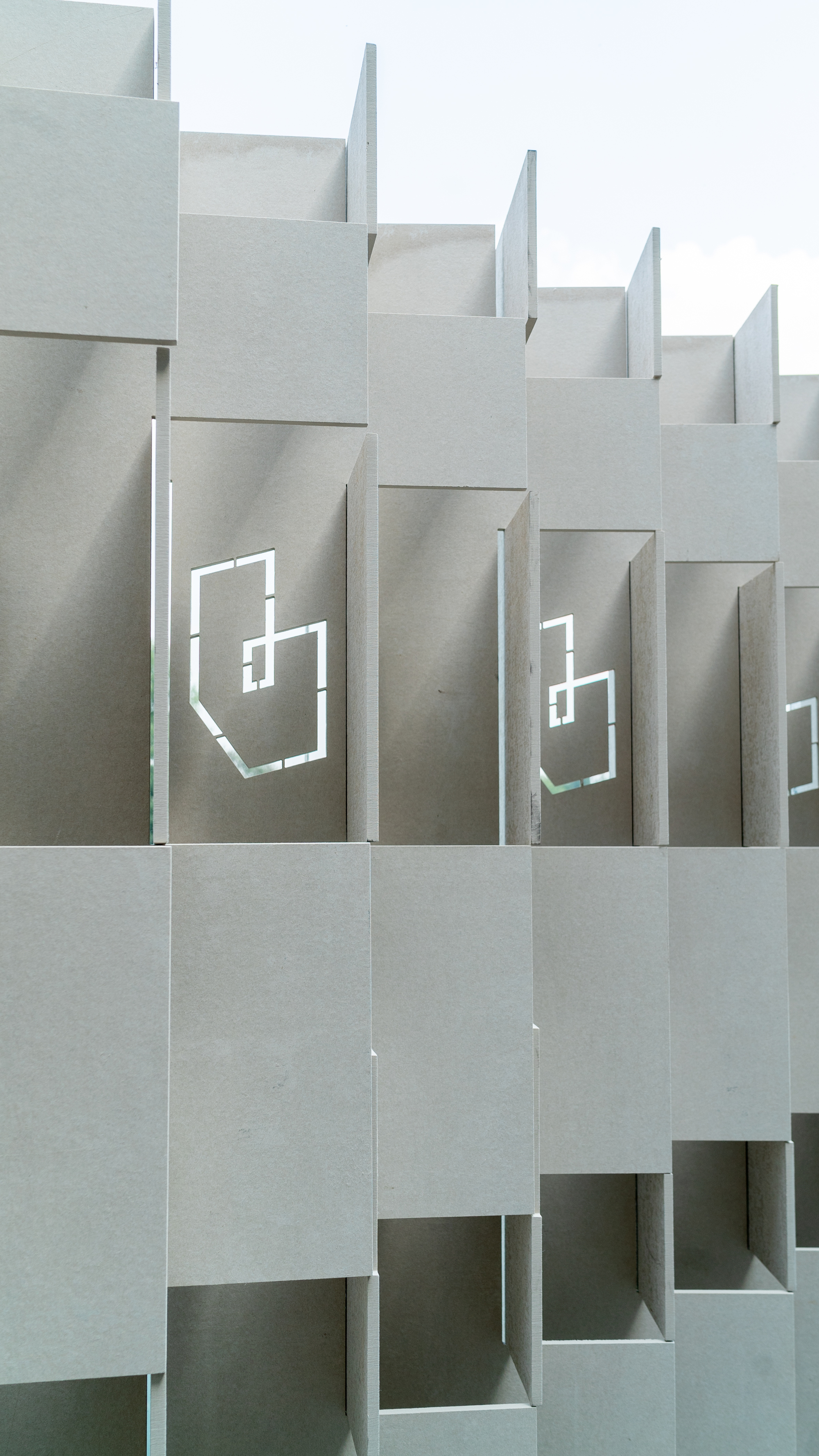 Stepped facade featuring staggered concrete volumes with recessed geometric logo cutouts under overcast sky
