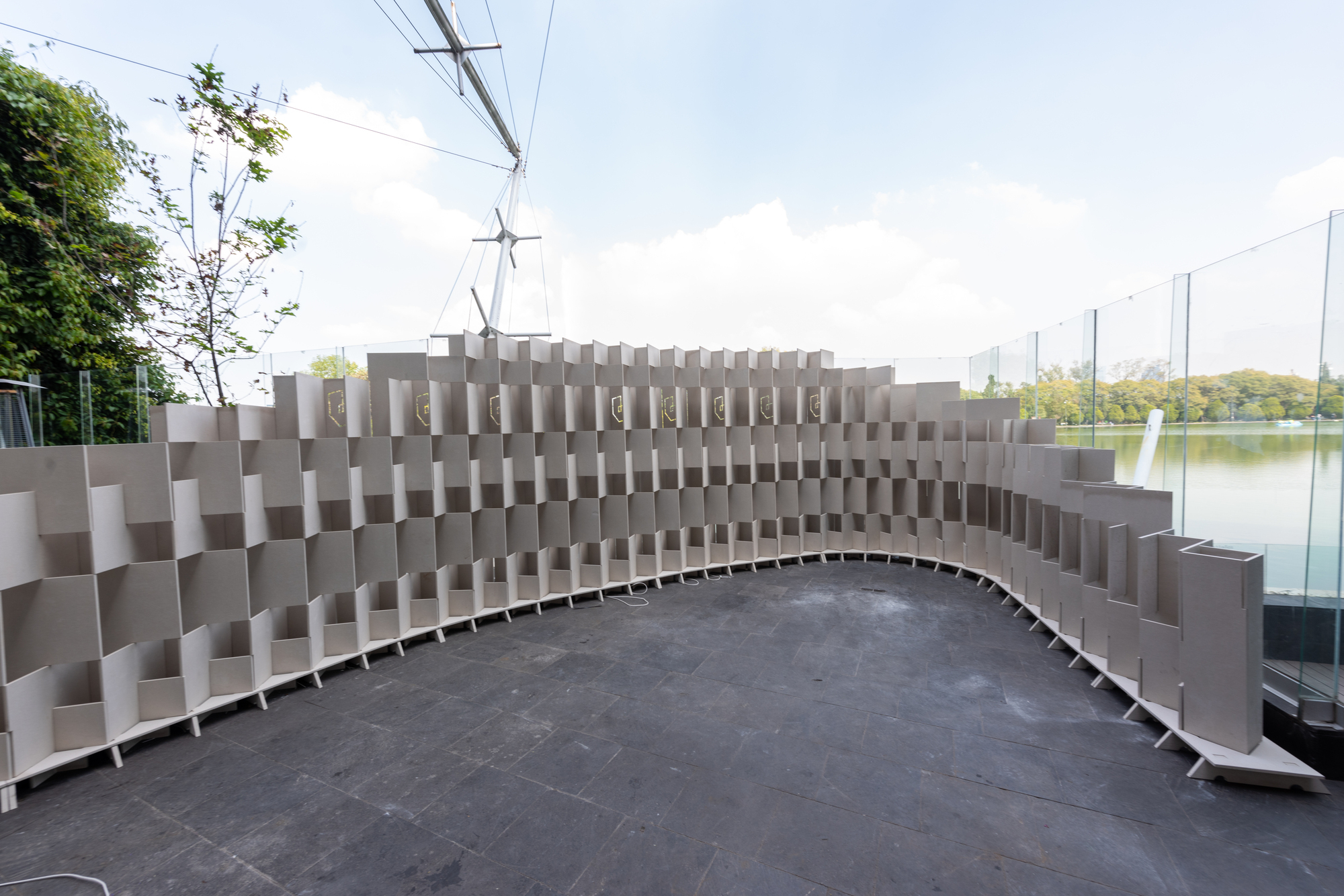 Curved grey modular seating wall with a pixelated surface pattern overlooking a pond with trees