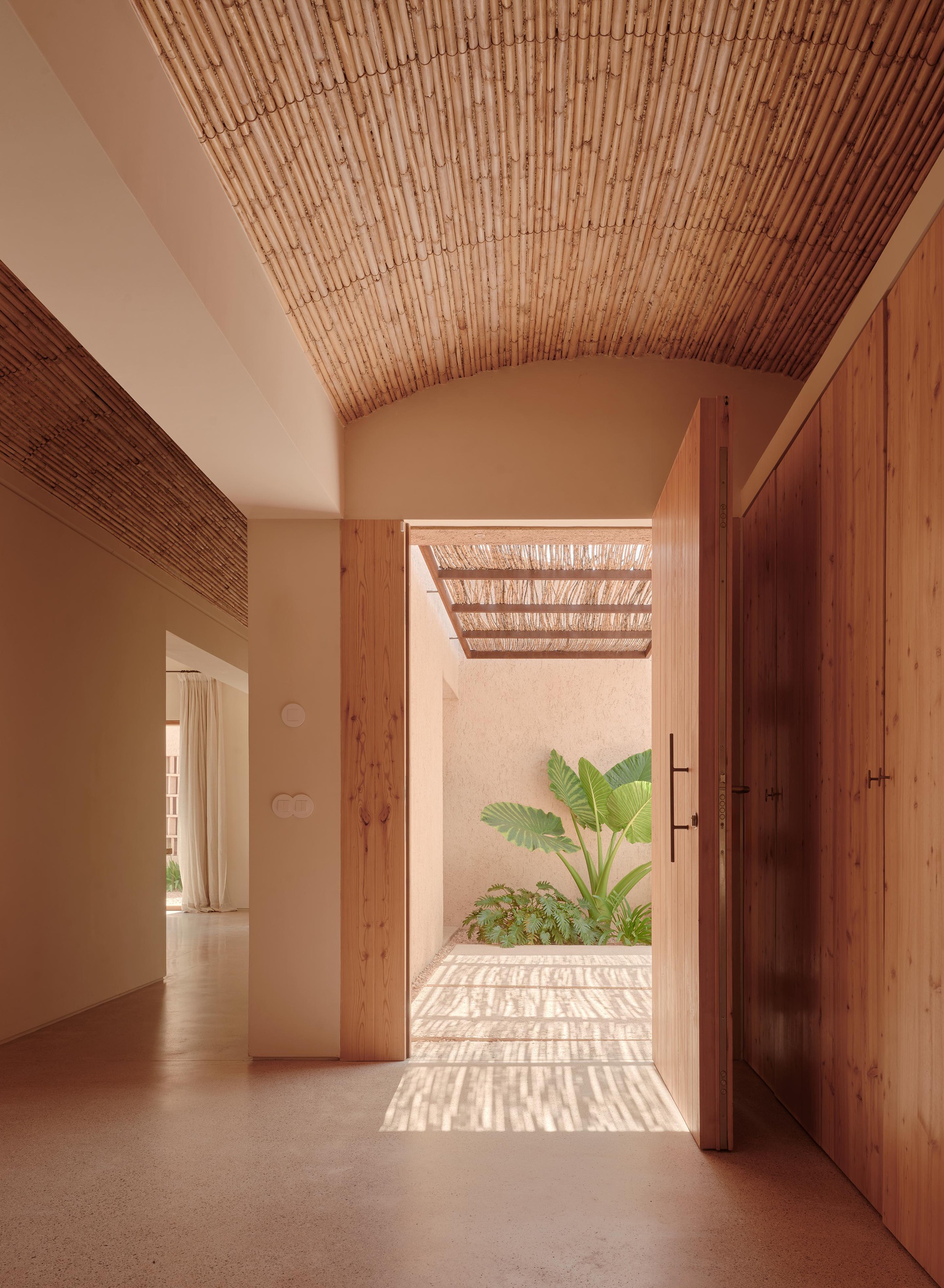 Interior hallway with vaulted slatted ceiling framing view to courtyard garden with dappled shadow