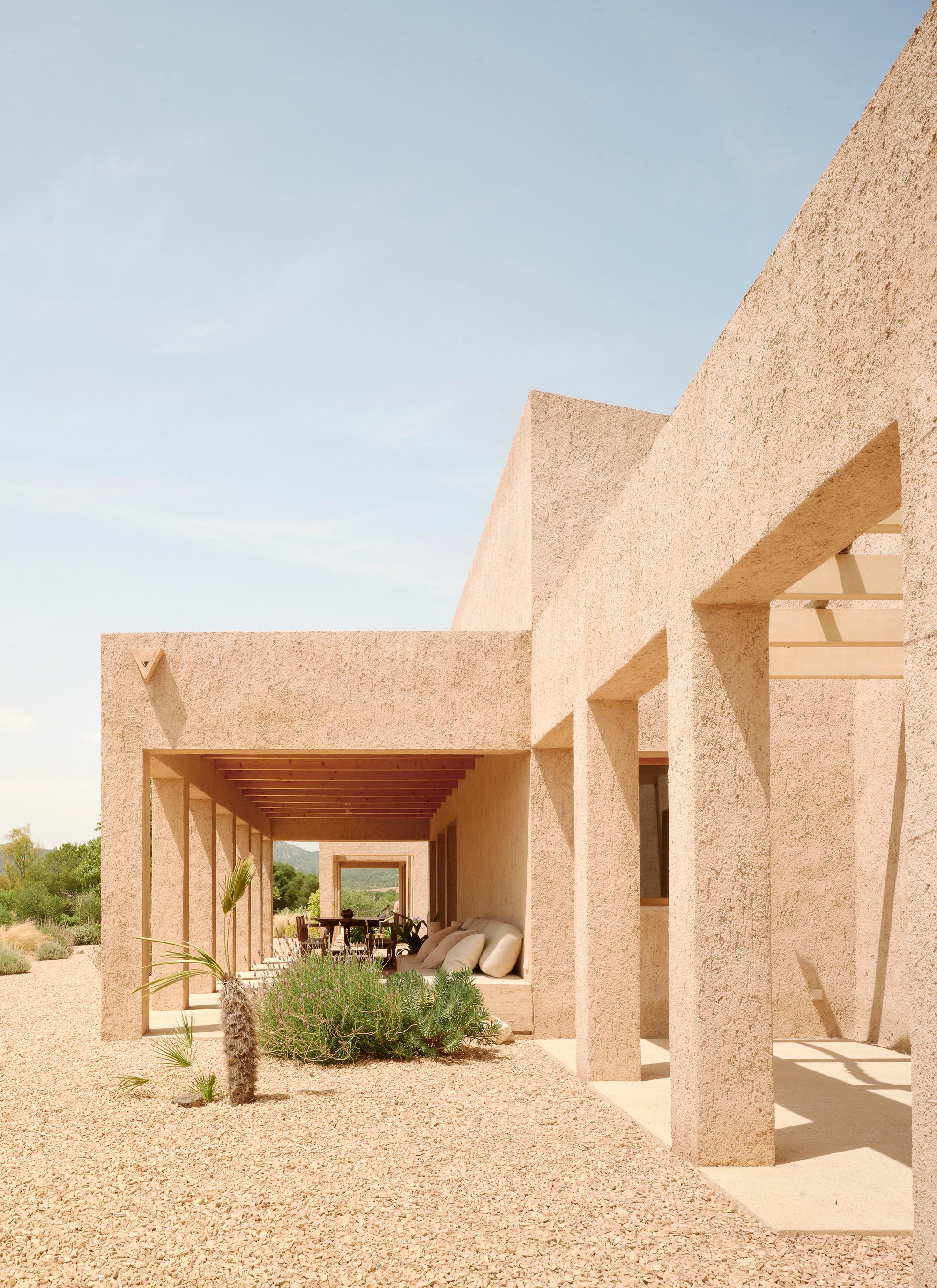 Open timber-beam loggia revealing furnished terrace and distant mountains through aggregate columns