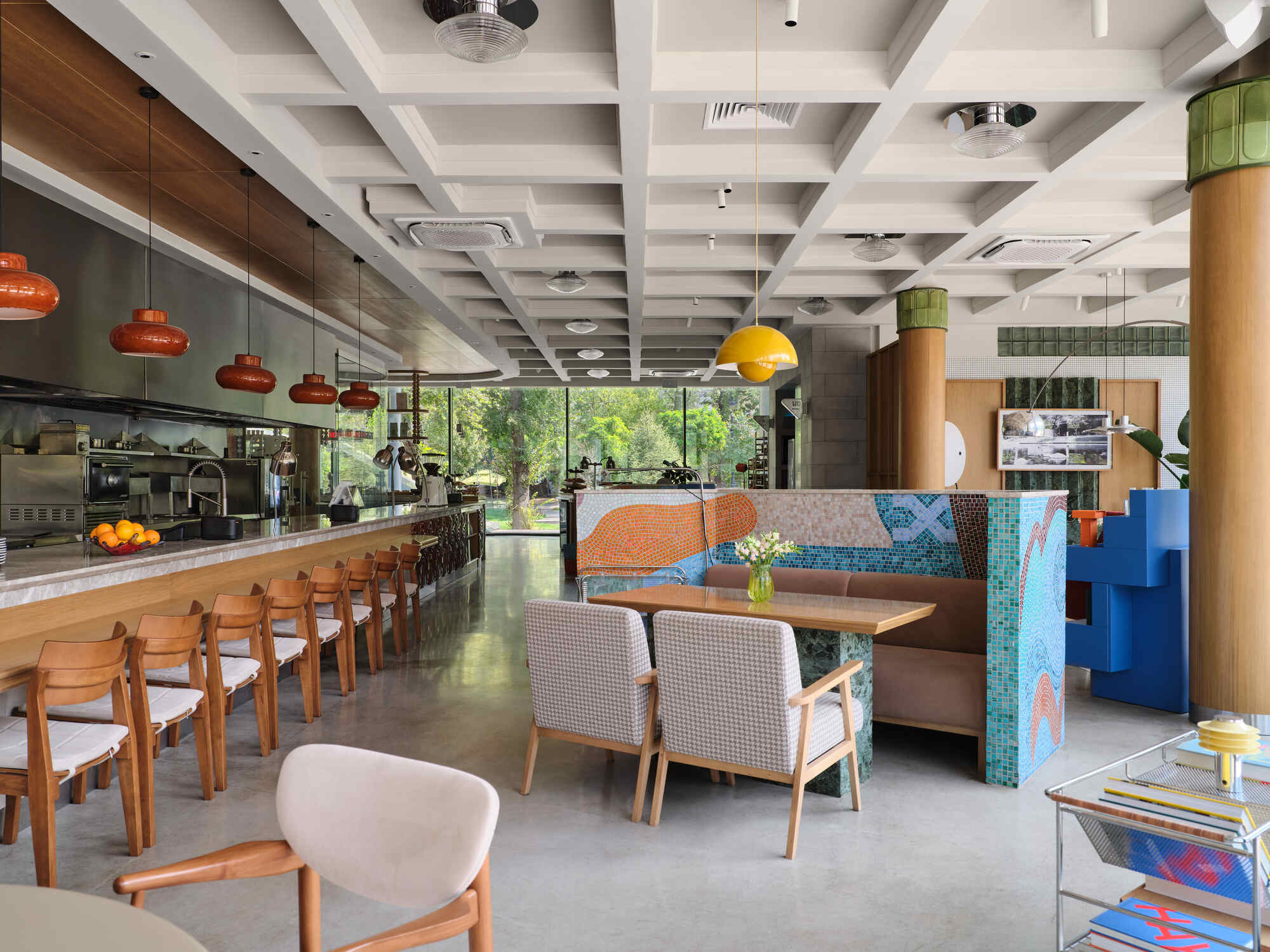 Open dining space with coffered white ceiling, cylindrical timber columns, and floor-to-ceiling glazing overlooking greenery