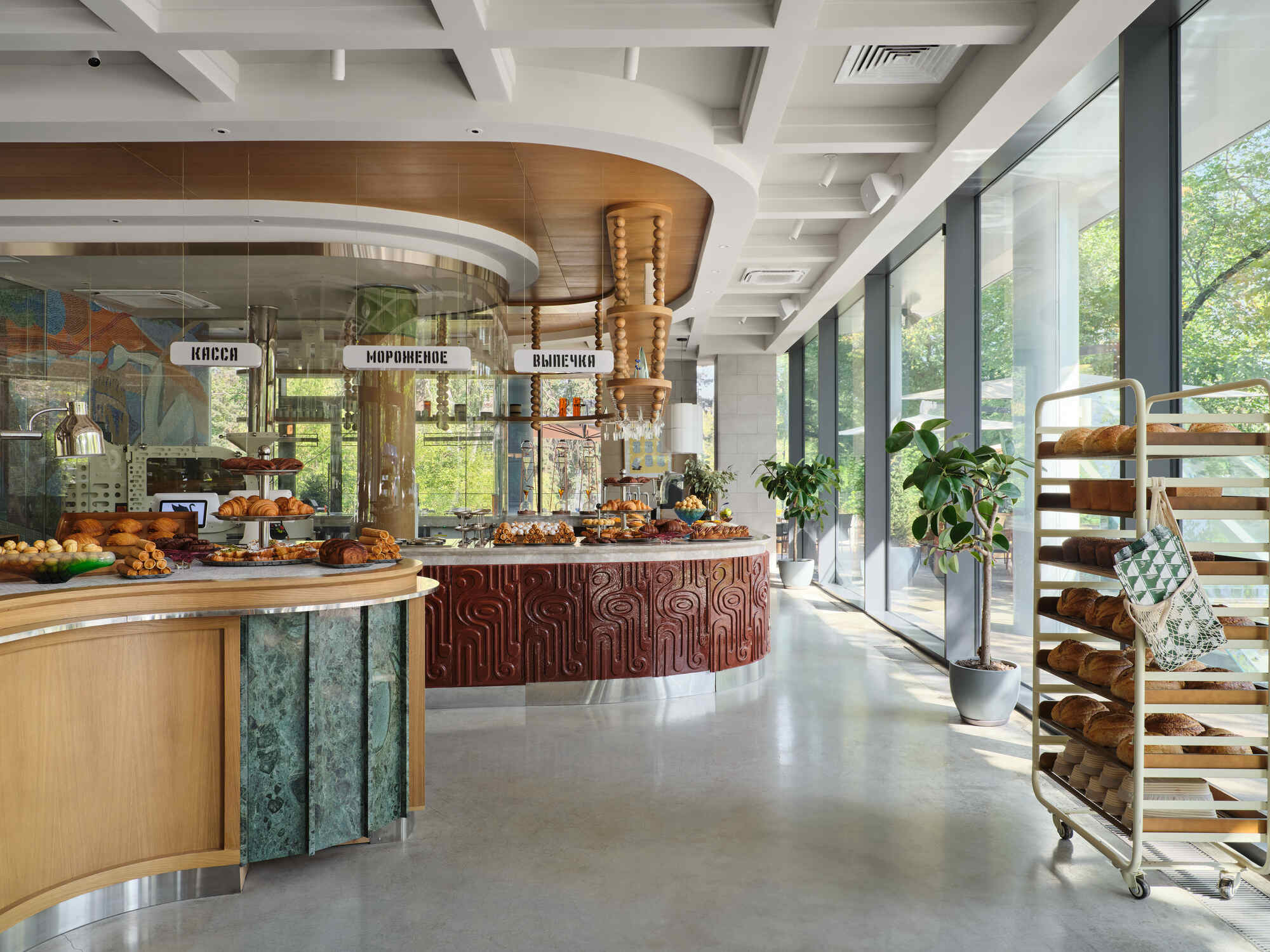 Bakery display counter clad in carved timber panels beneath a cylindrical timber column with pendant lights