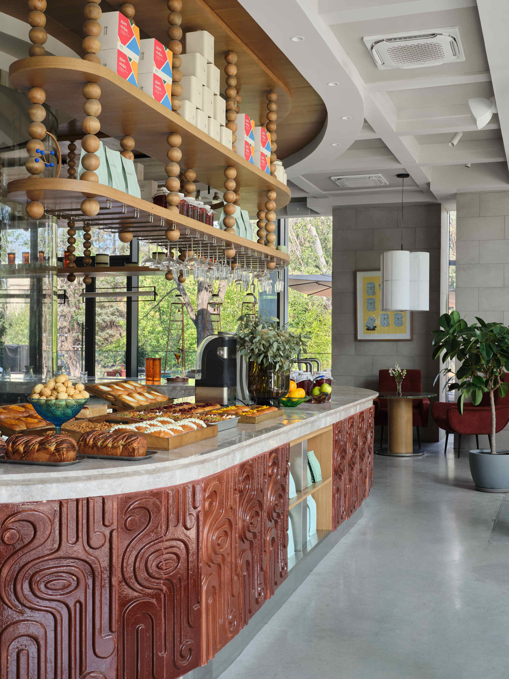 Curved bakery counter with carved timber cladding beneath a suspended shelf with wooden beads