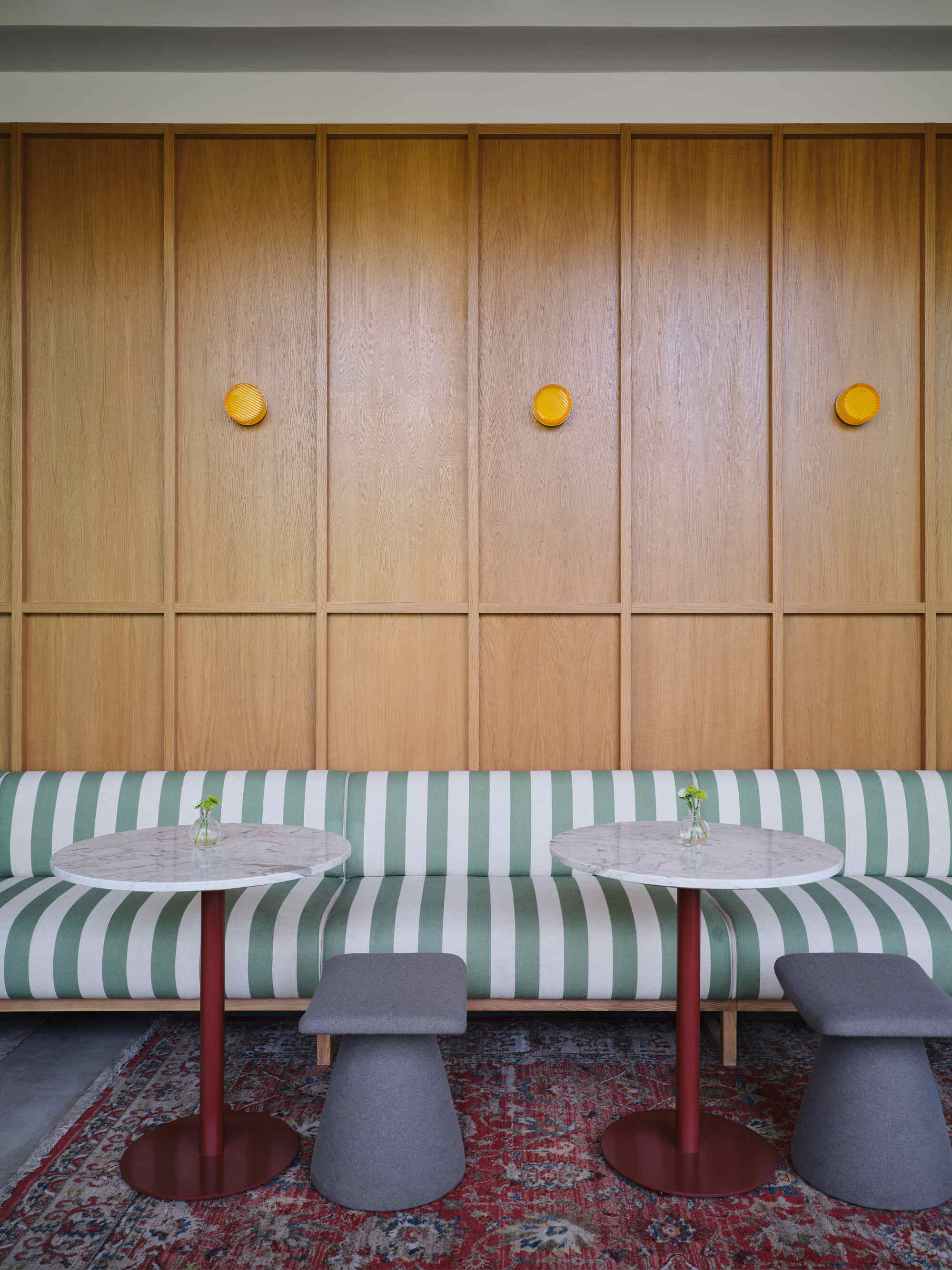 Built-in banquette with green and white striped upholstery below timber wall panels with yellow circular knobs