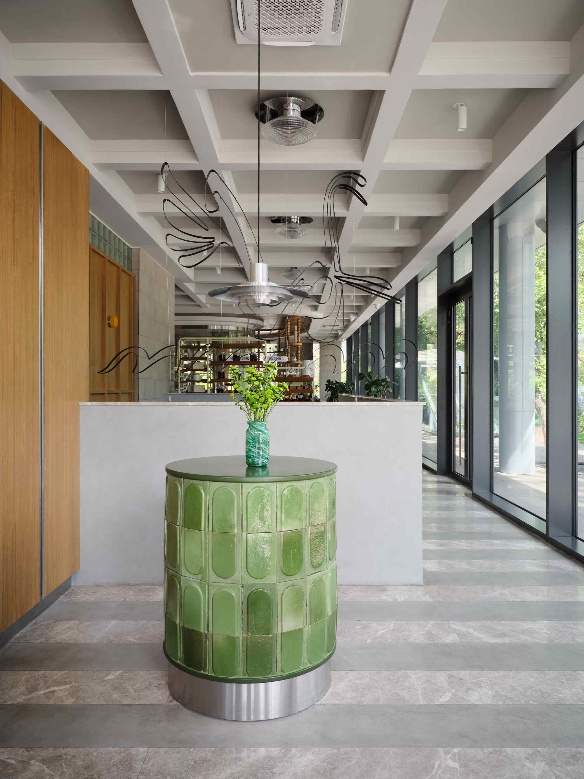 Green glazed tile pedestal in entrance area with coffered ceiling and sculptural pendant fixture overhead
