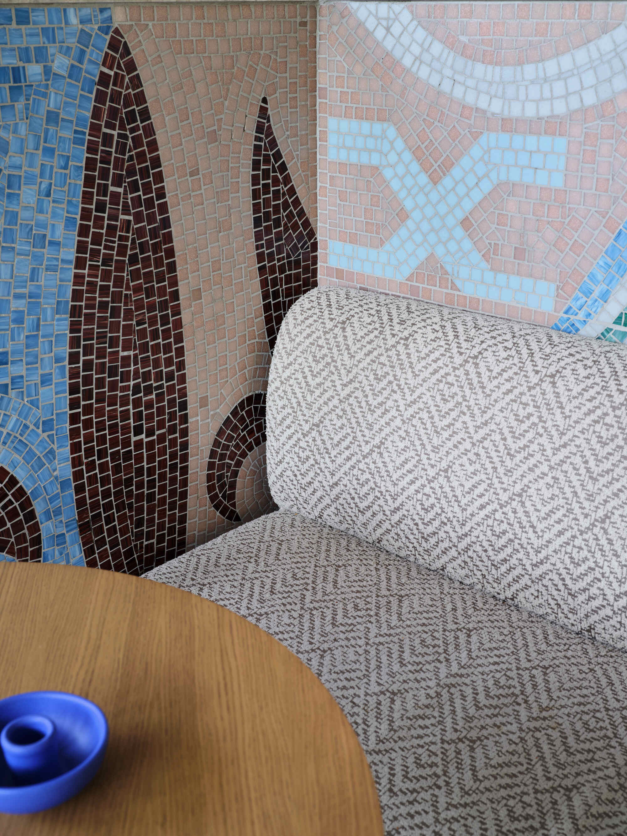 Corner seating with chevron upholstery against colorful mosaic wall featuring cypress tree motifs in blue and brown
