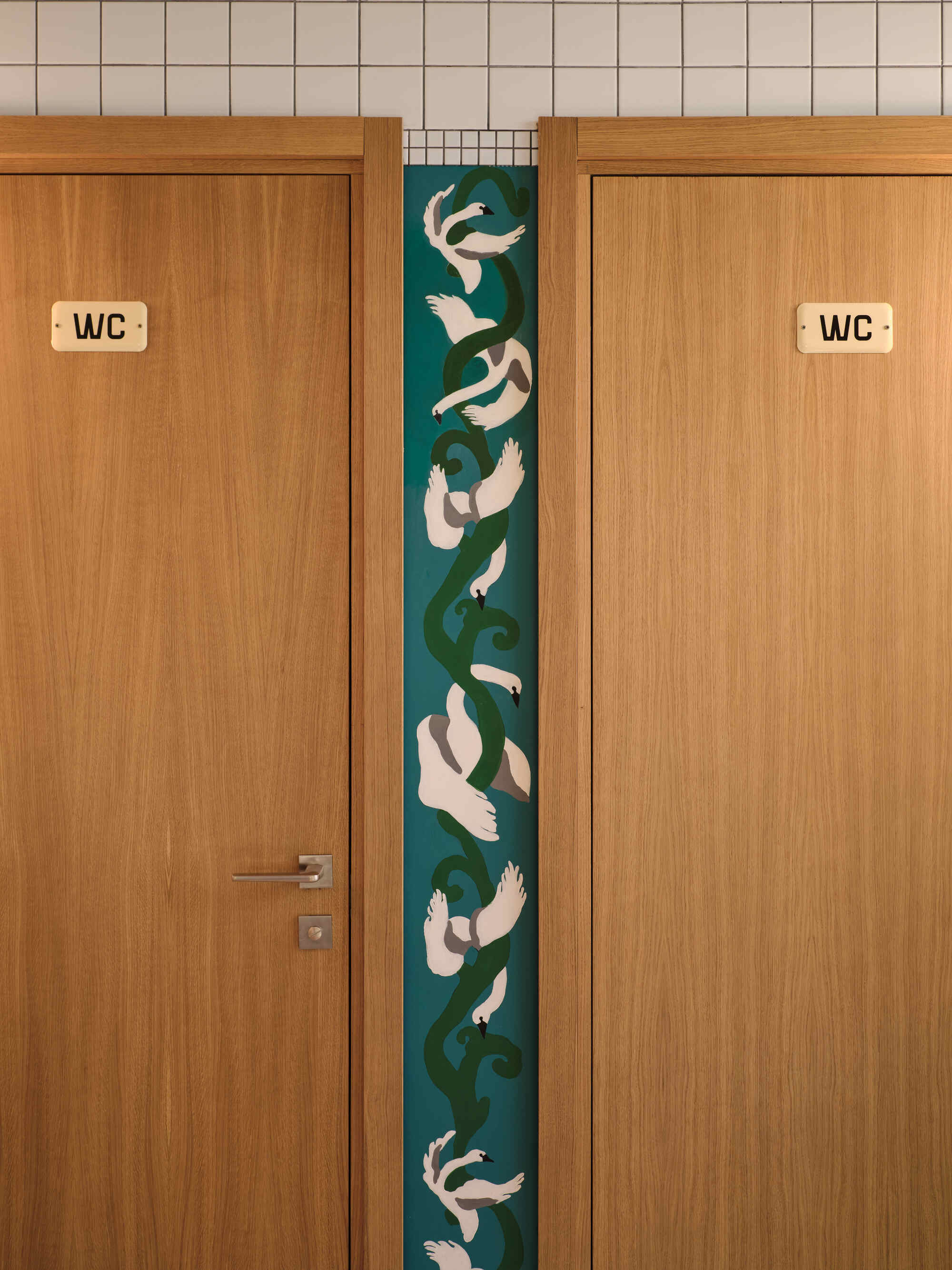 Pair of oak restroom doors flanking a vertical tile panel with koi fish mosaic in blue and green