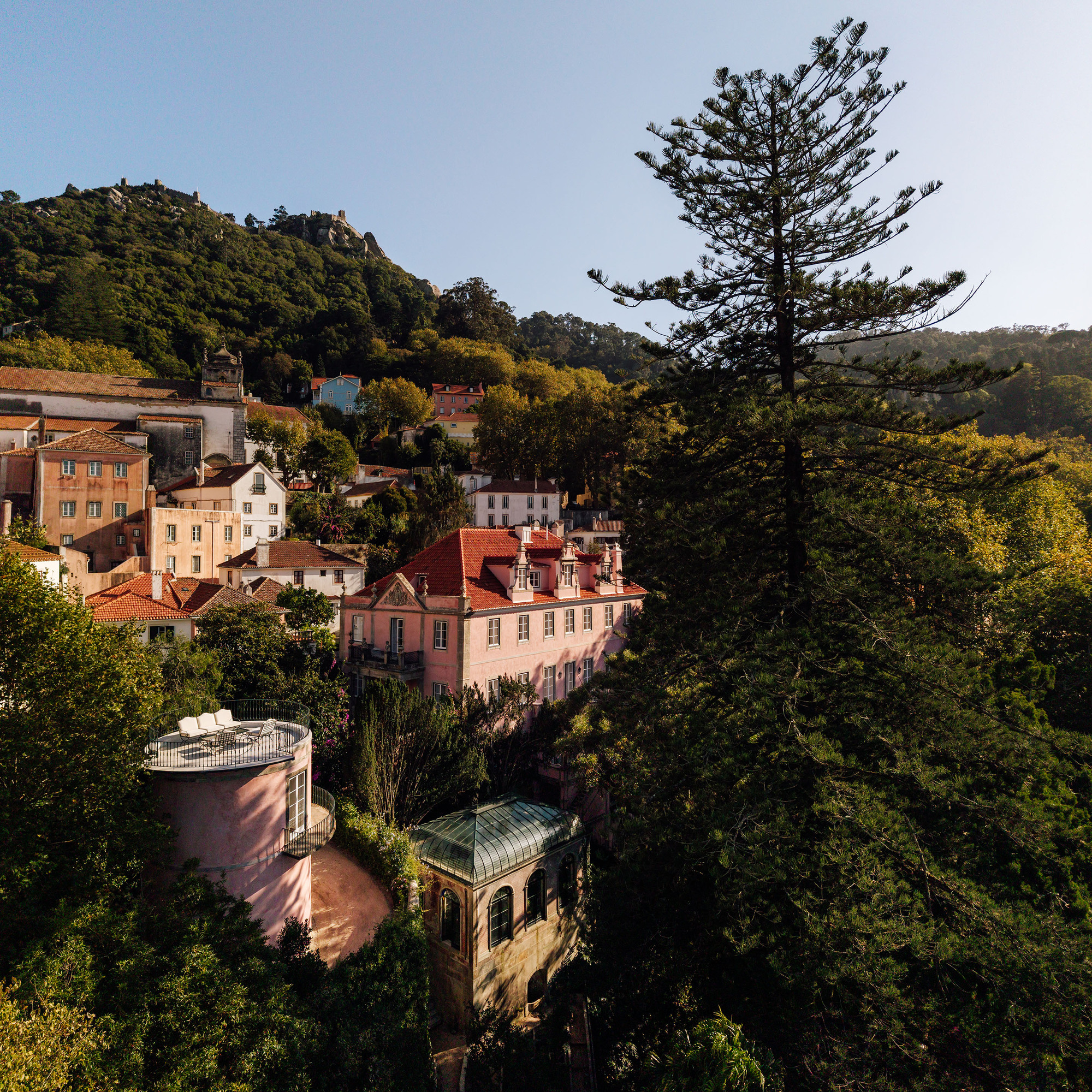 Aerial view of terraced structures with tiled roofs and a glass conservatory nestled among hillside trees