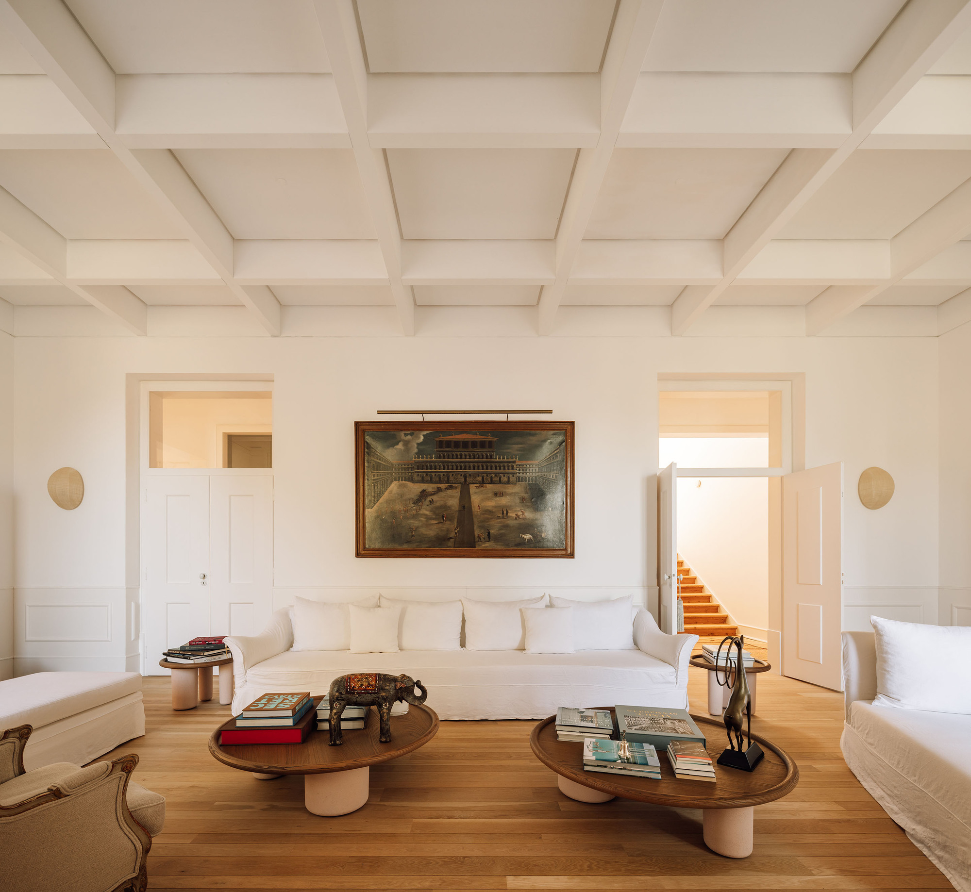 White coffered ceiling above a salon with timber floors and symmetrical doorways flanking a framed painting
