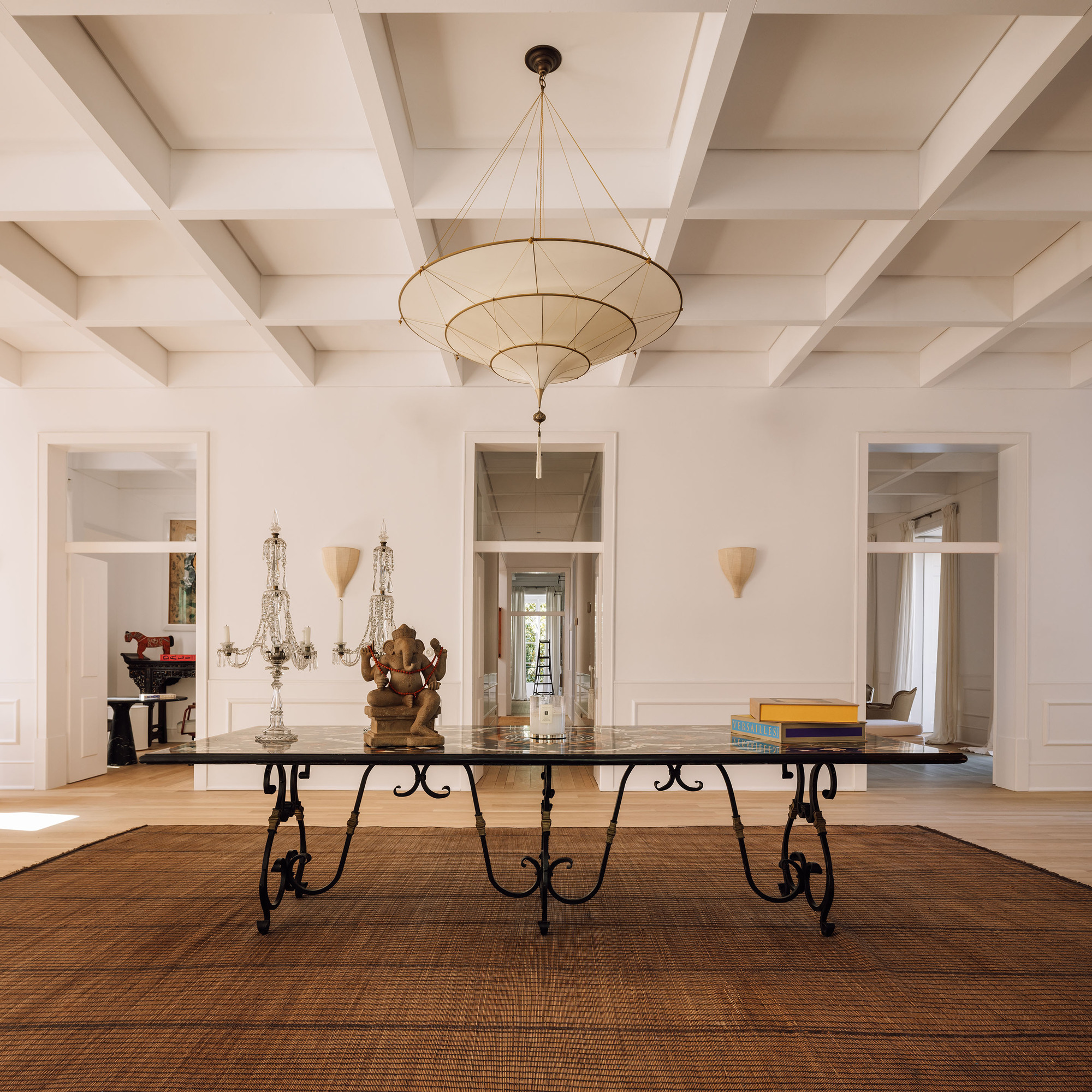 Dining room with coffered ceiling and tiered pendant fixture above a marble table with iron legs