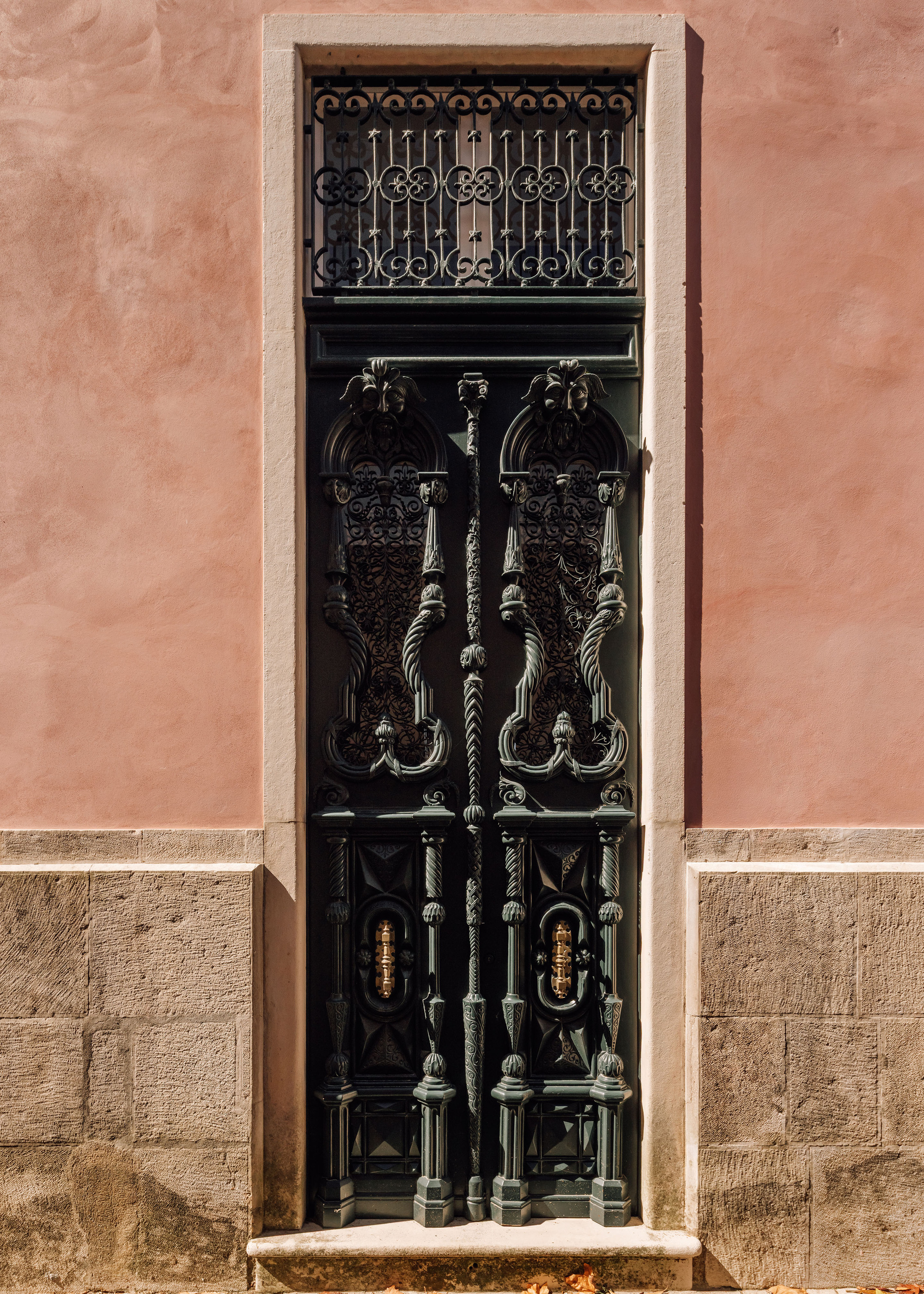 Black ornamental metalwork door with transom grille set in a stone and plaster facade
