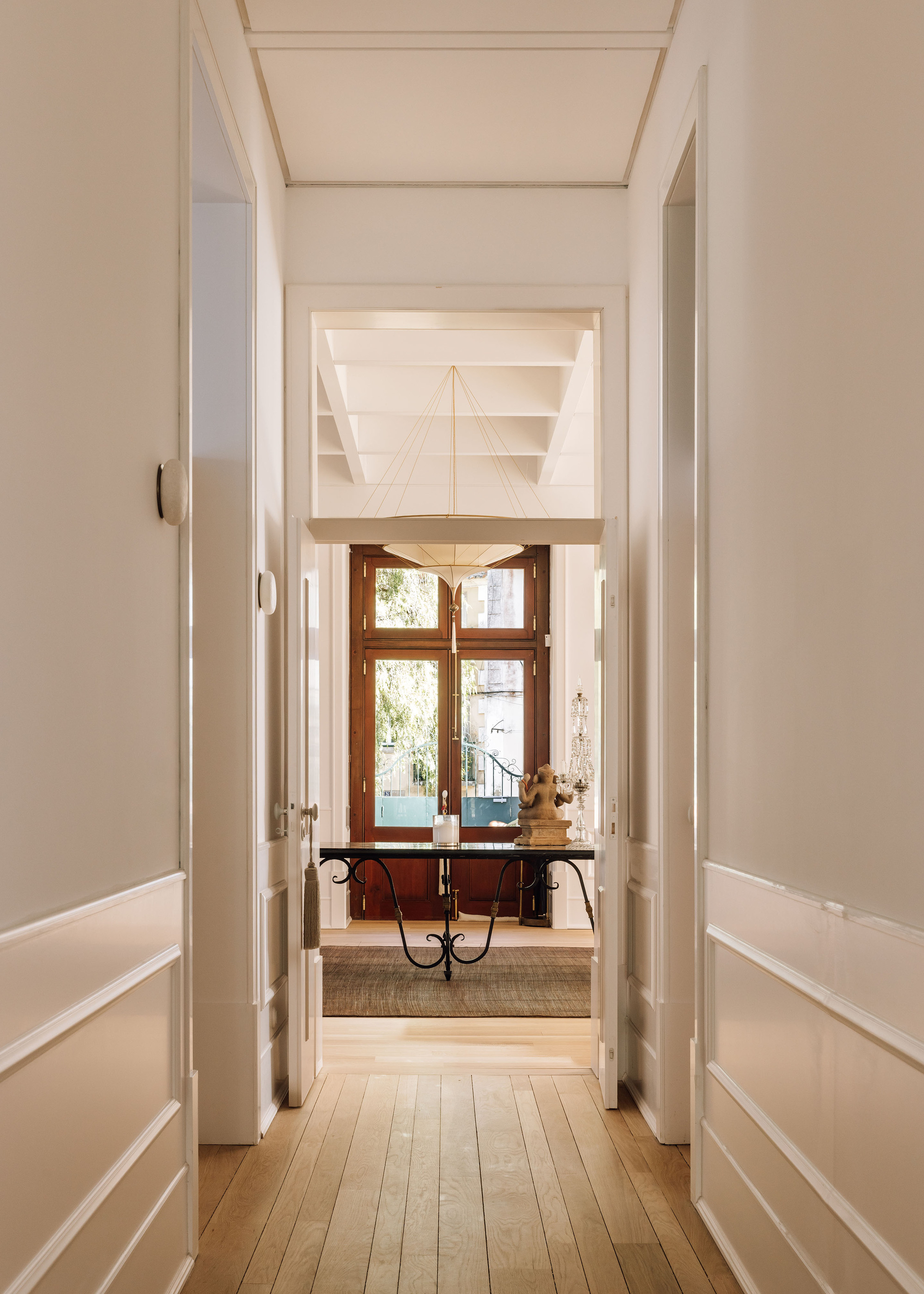 Axial view through white paneled hallway toward timber console table beneath a window with daylight